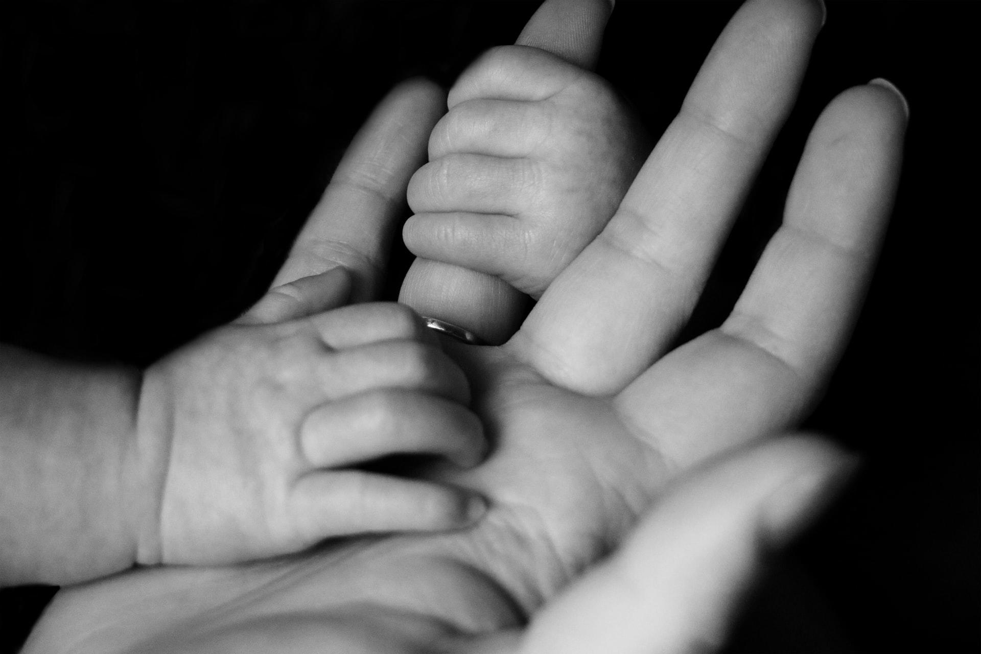 Die Hände eines Babys halten sich an der Hand eines Erwachsenen fest.