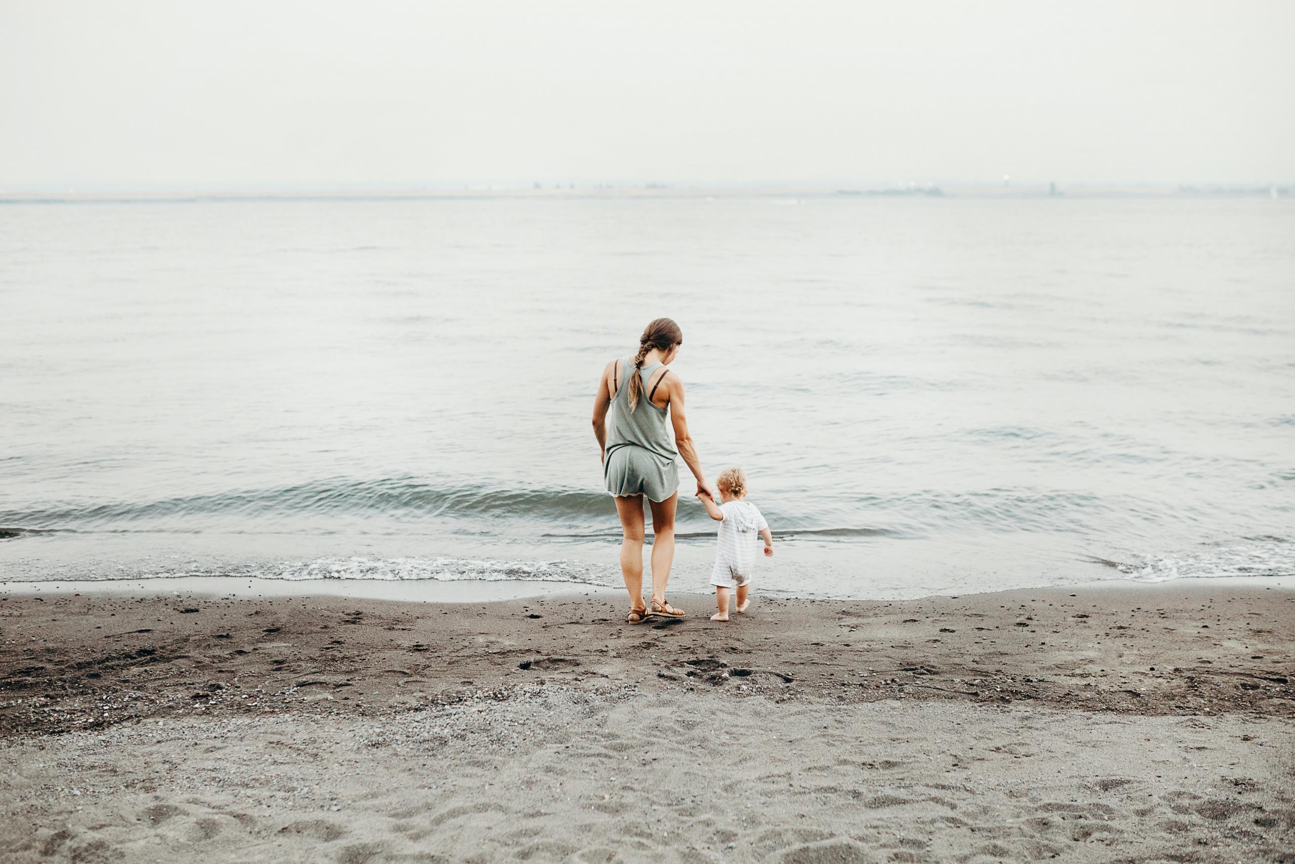 Eine Mutter und ihr Kleinkind laufen am Strand auf Meer zu.