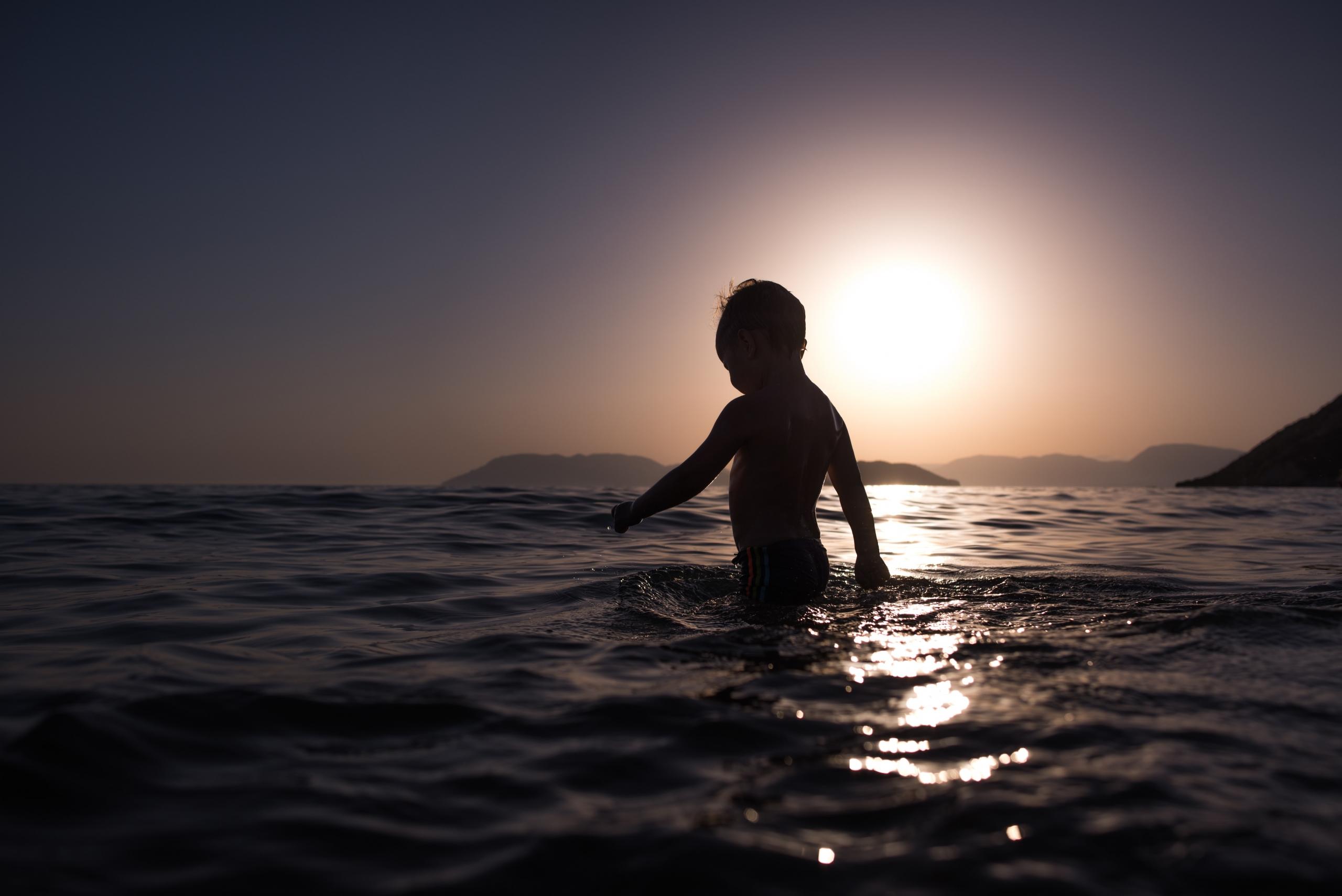 Im Sonnenuntergang läuft ein kleiner Junge in Hüfthöhe durchs Meer.