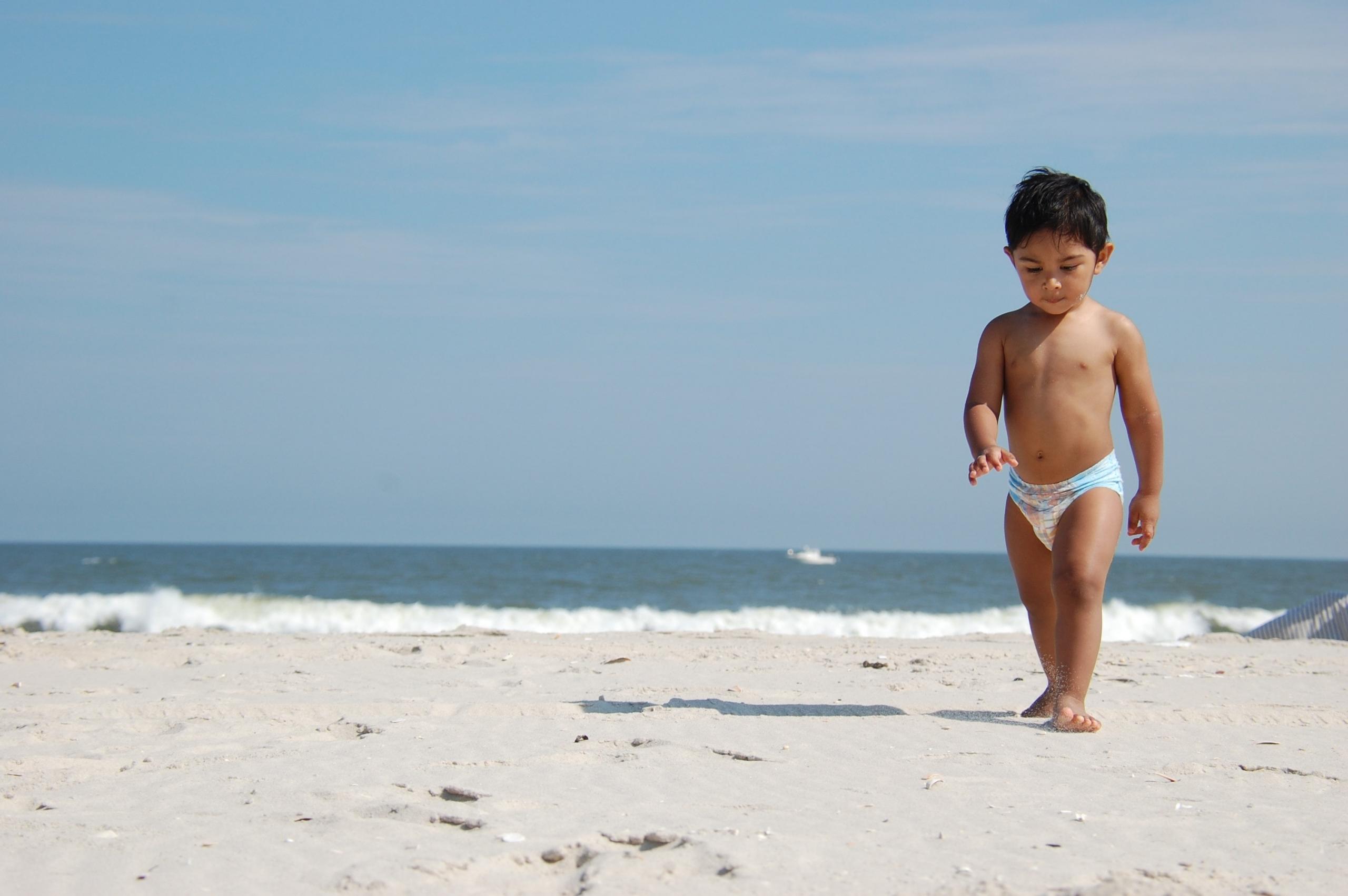 Am Strand läuft ein Kleinkind in Babywindel.