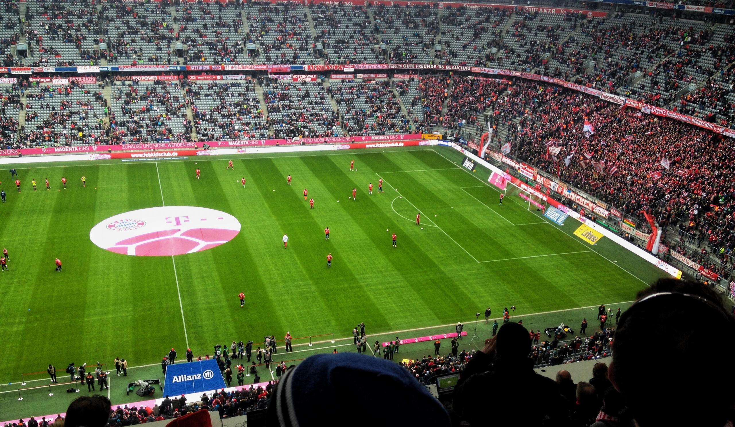 Die halb gefüllte Allianz Arena vor einem Fußballspiel. Während der Bundesliga Saison finden hier regelmäßig bis zu 75.000 Zuschauer Platz.