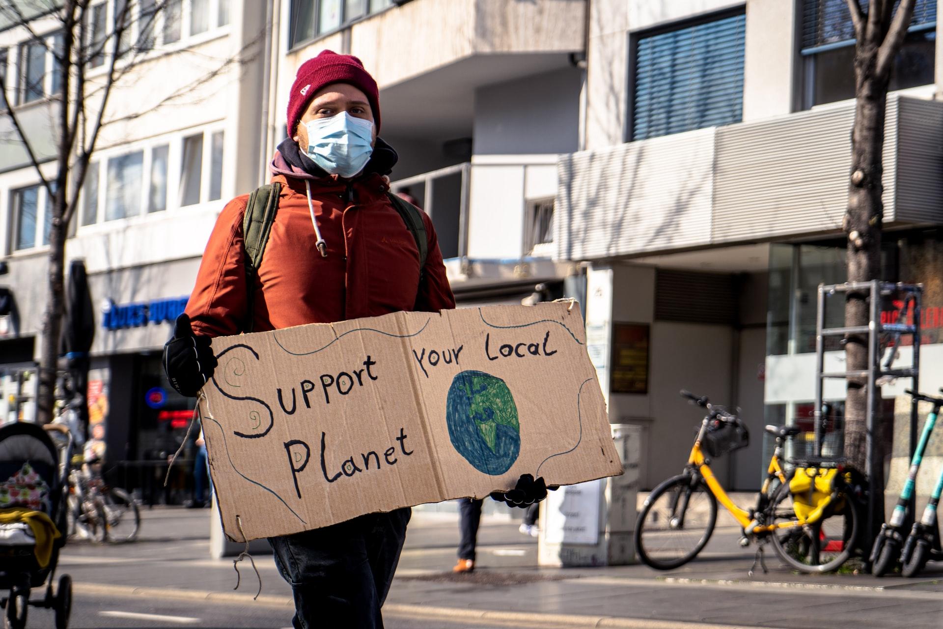 Ein Demonstrant auf einer Demonstration trägt eine Maske und hält ein Schild in der Hand mit der Aufschrift Support your local planet