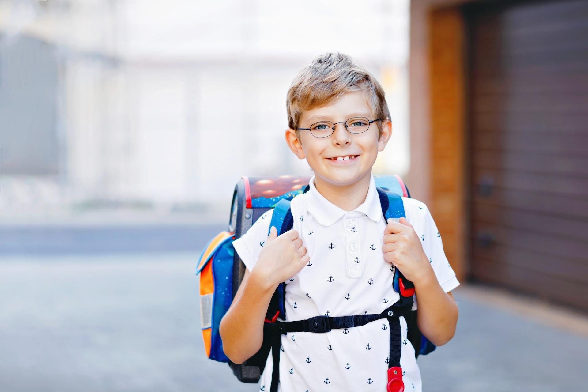 Ein lächelnder Junge trägt einen Schulranzen auf dem Rücken