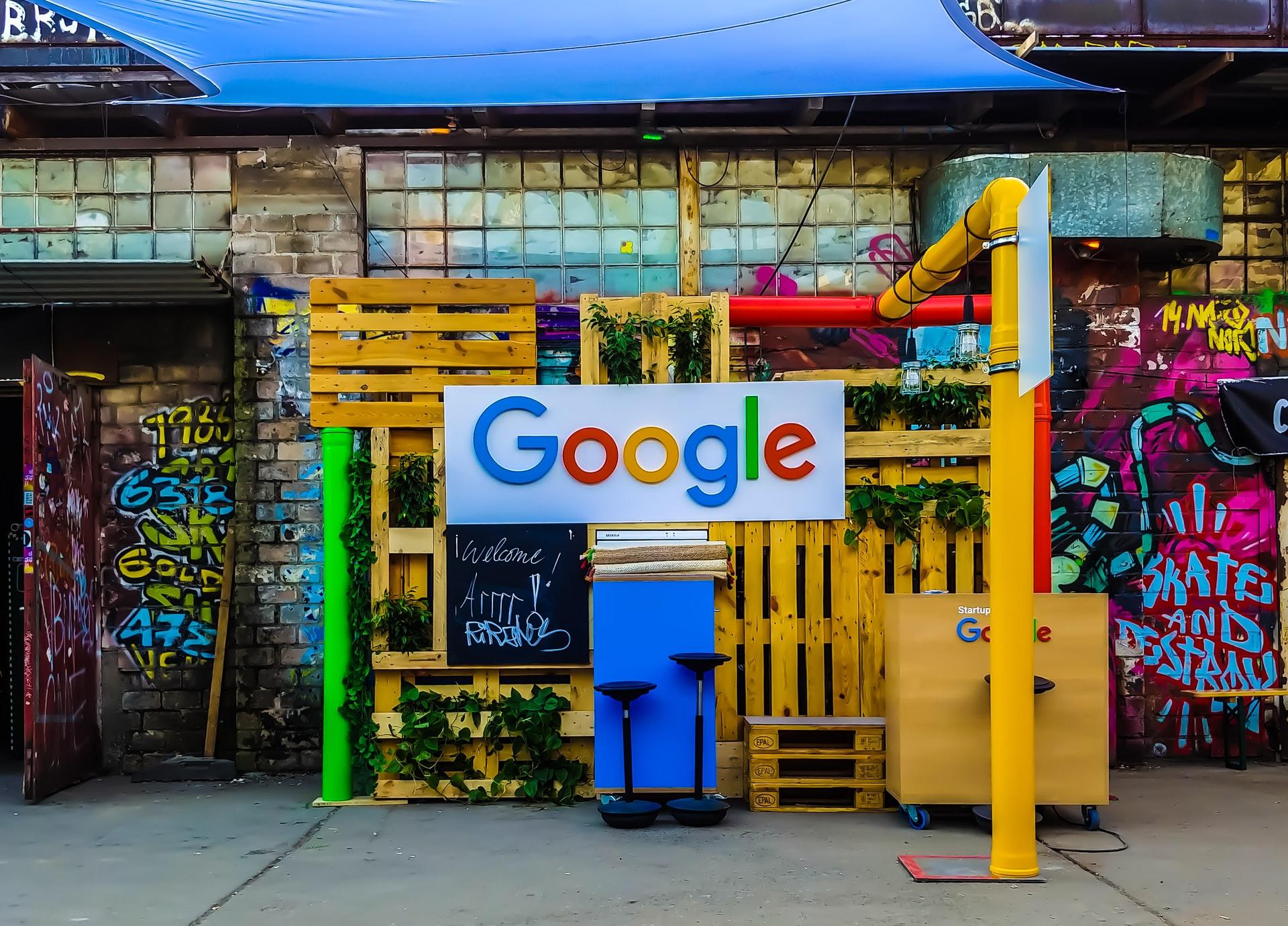 Vor einem bunten Gebilde aus Holzpaletten ist das Google-Logo angebracht.