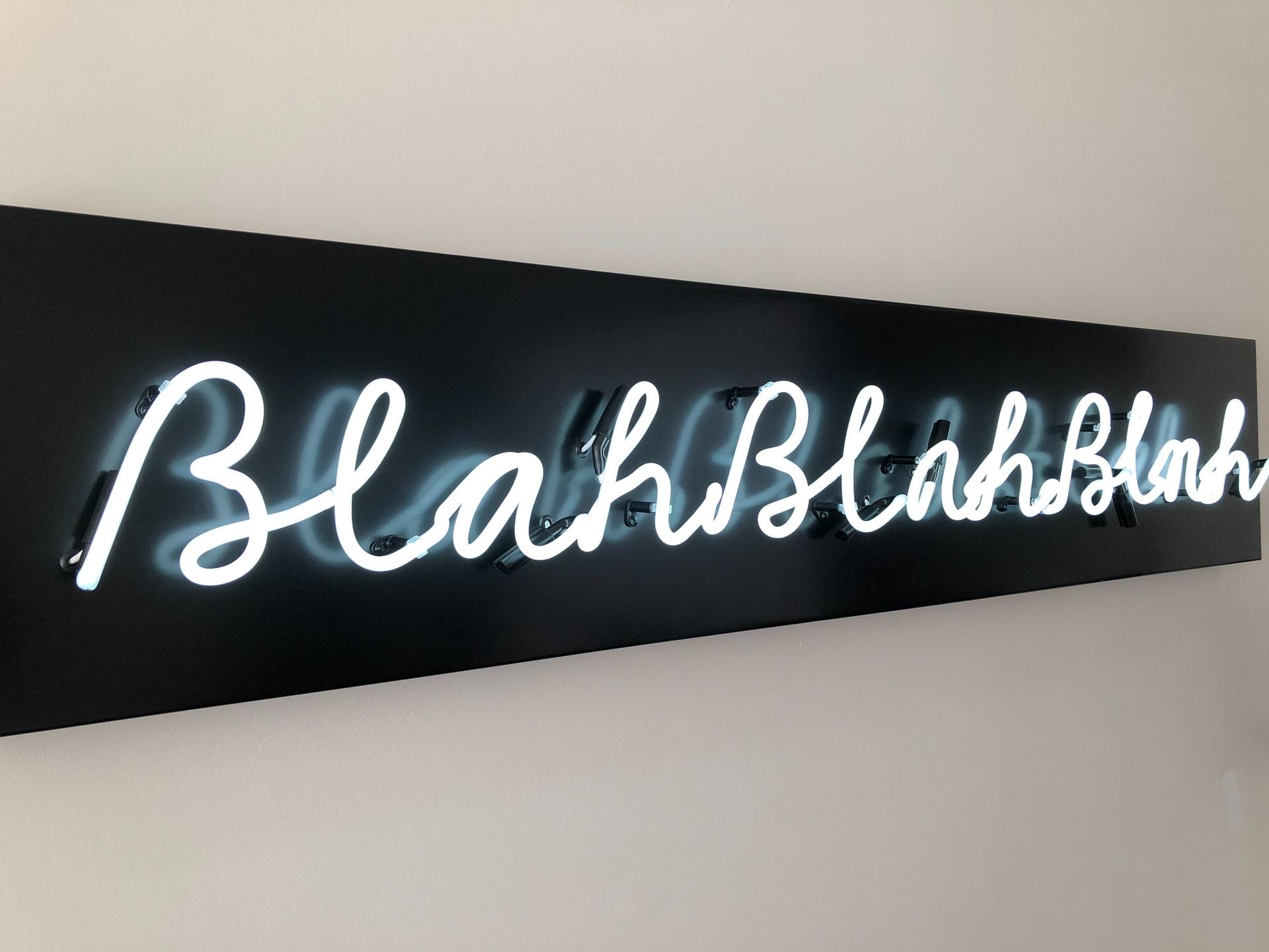 An einer weißen Wand hängt ein leuchtender Schriftzug blahblahblah vor schwarzem Hintergrund