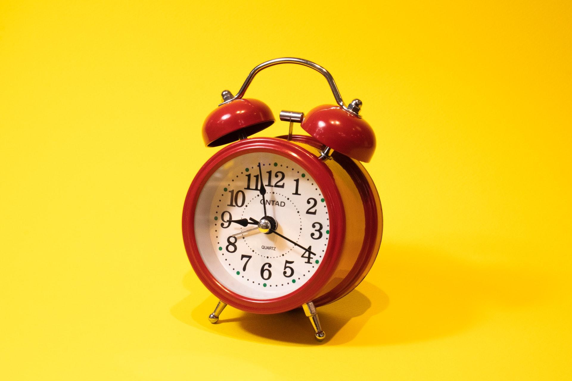 Auf einem roten Wecker vor gelbem Hintergrund stehen die Zeiger auf kurz vor neun Uhr.