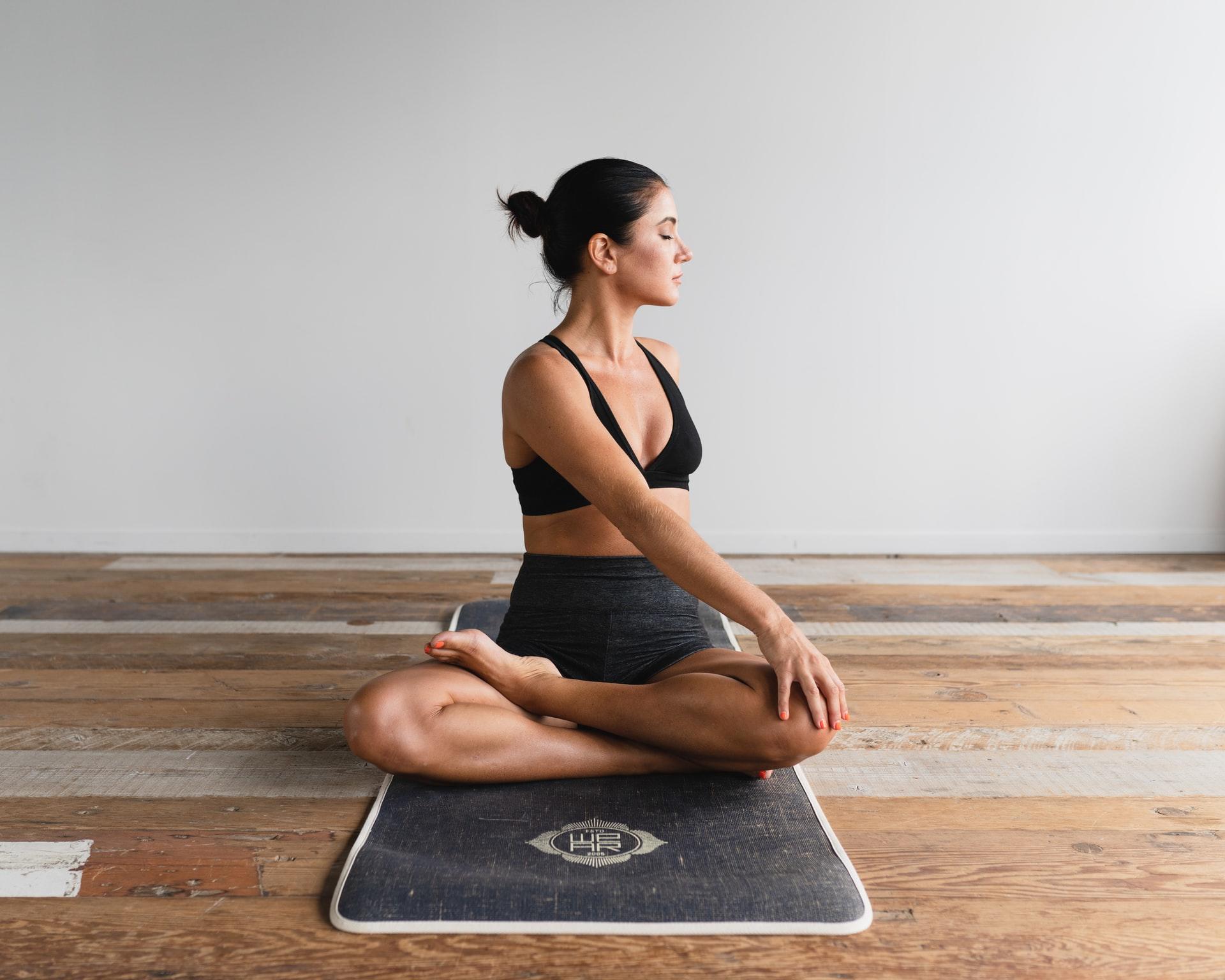 Eine Frau sitzt auf einer Matte auf einem Holzboden und macht Yoga.