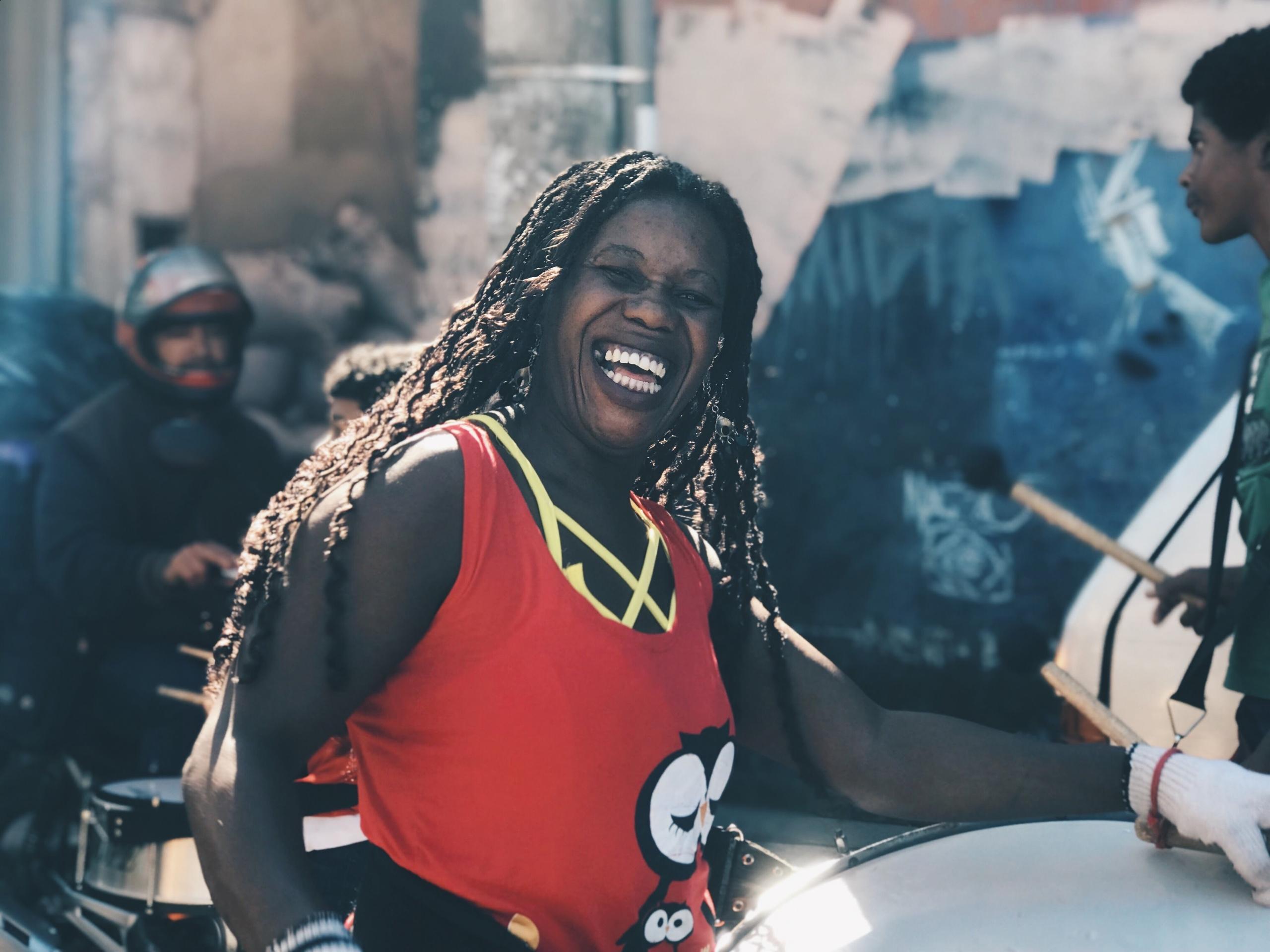 Eine Frau afrikanischen Ursprungs mit einer grossen Trommel vor sich strahlt in die Kamera.