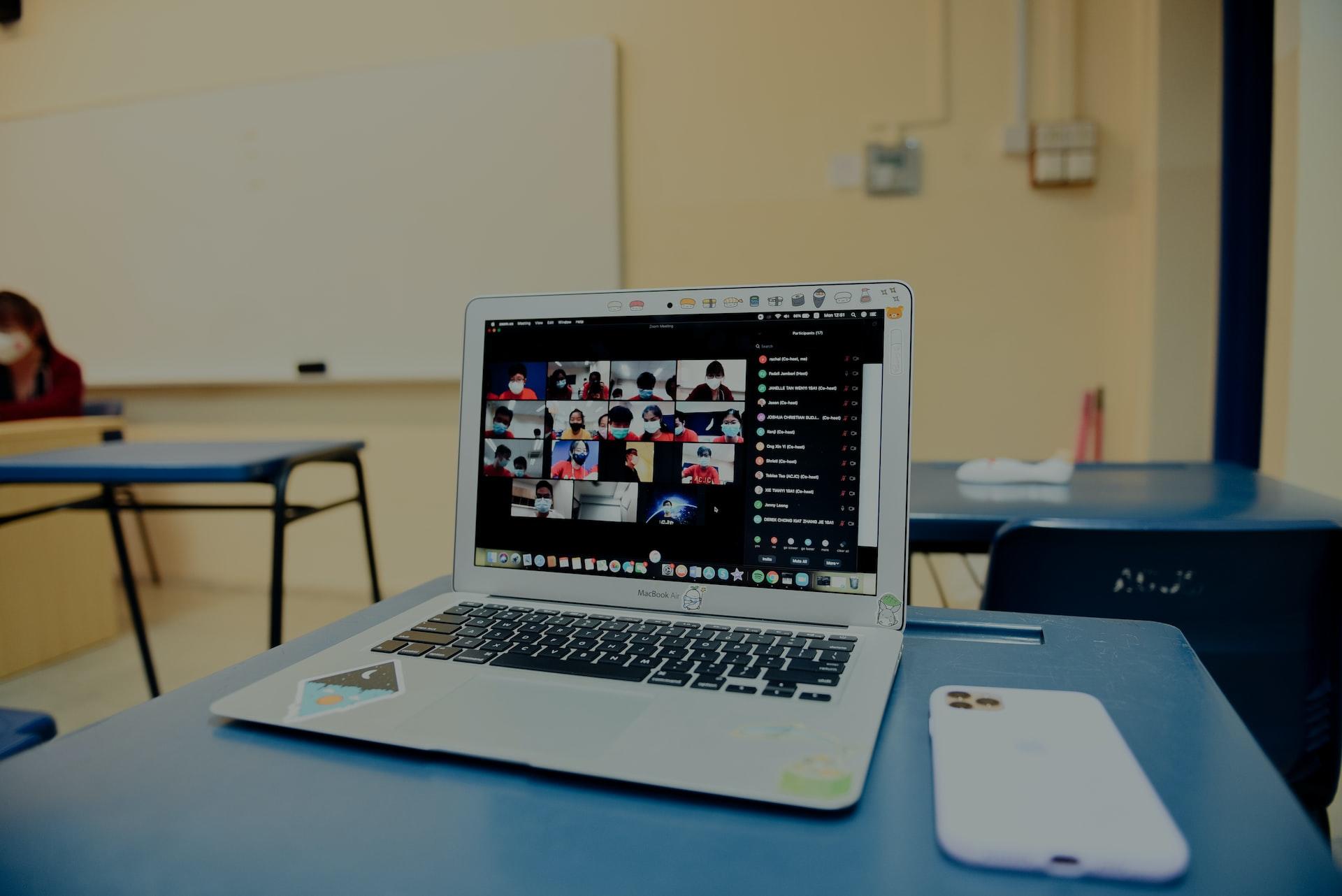 Auf einem Tisch steht ein geöffneter Laptop und mehrere Personen sind auf dem Bildschirm.
