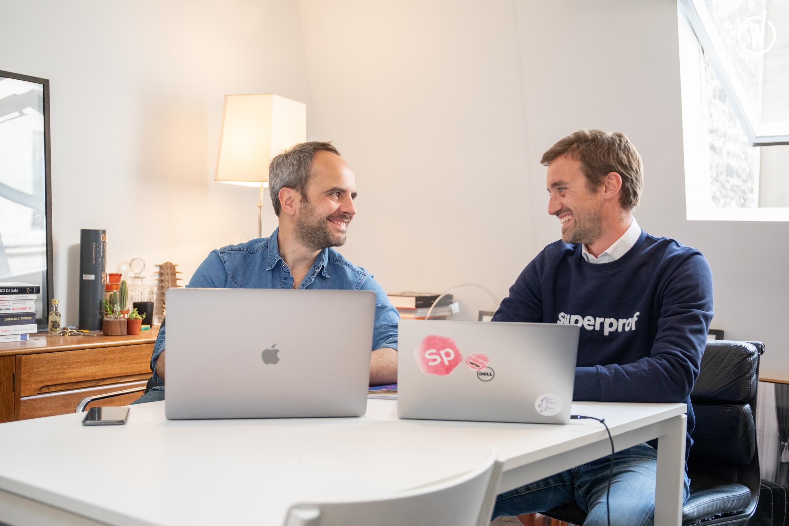 Die beiden Gründer von Superprof sitzen an ihren Laptops und lachen sich an.