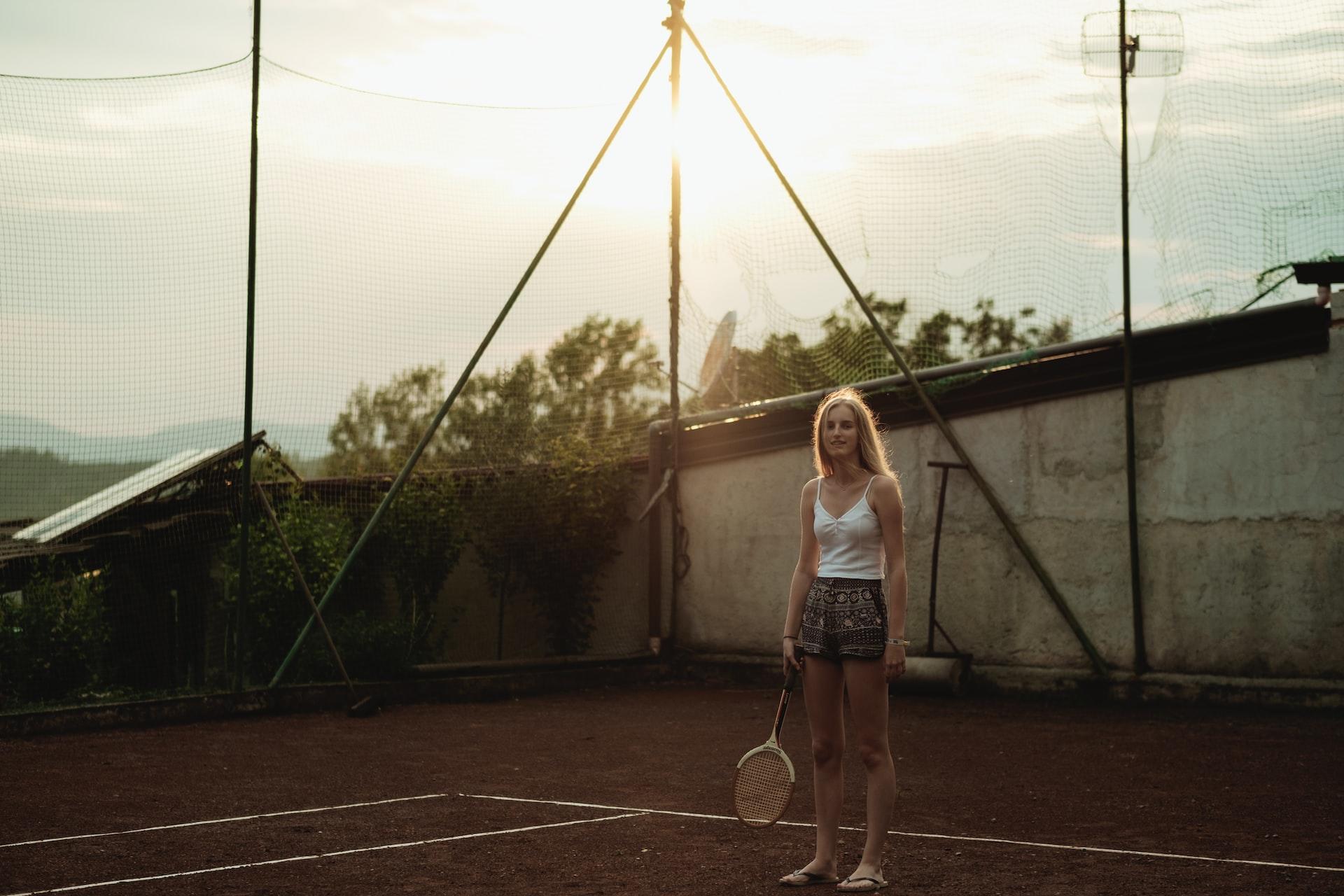 Eine Frau steht während der Dämmerzeit auf dem Tennisplatz mit einem Tennisschläger in der Hand