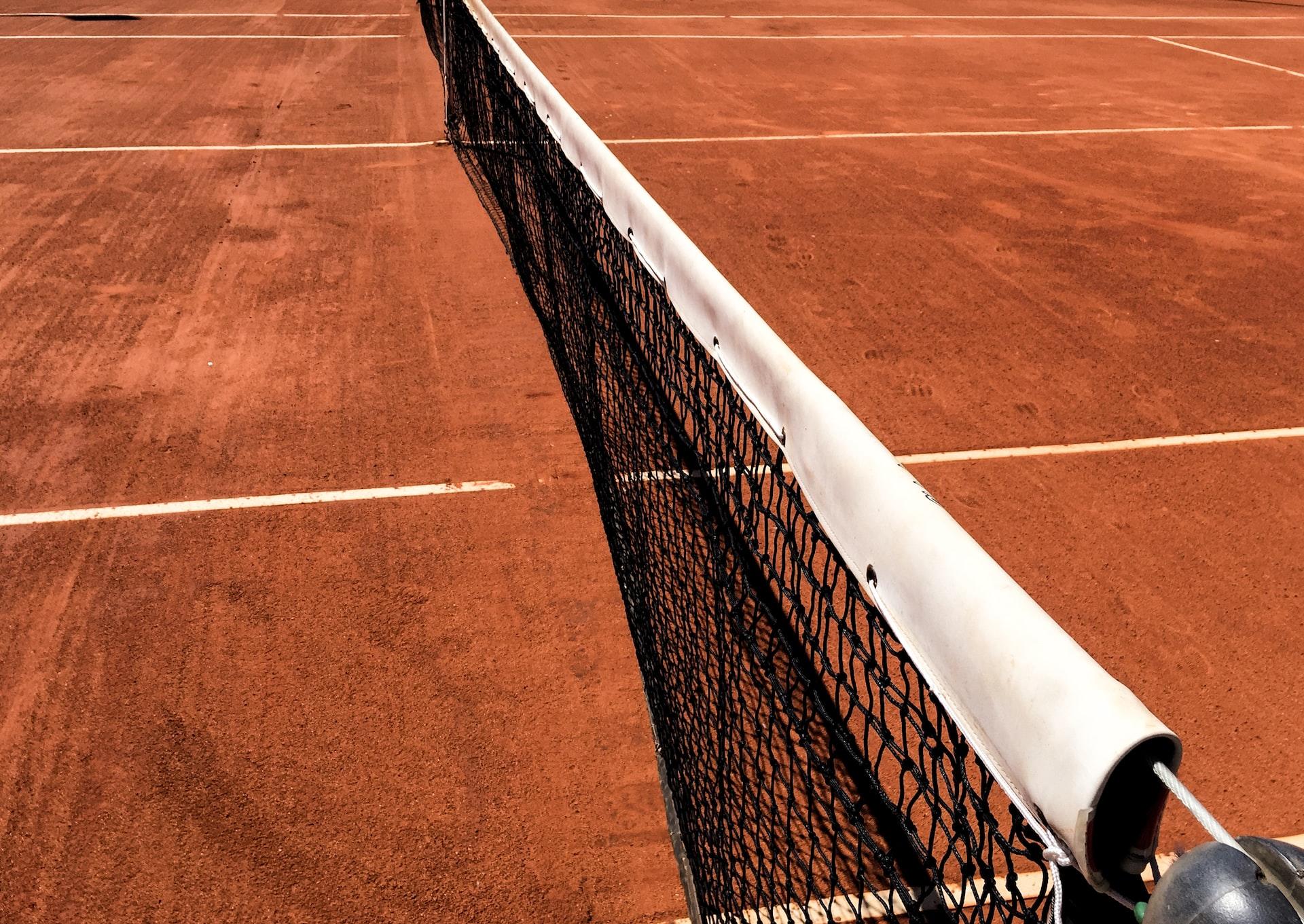 Aufnahme eines Tennisplatzes mit rotem Sand rechts und links neben dem Netz