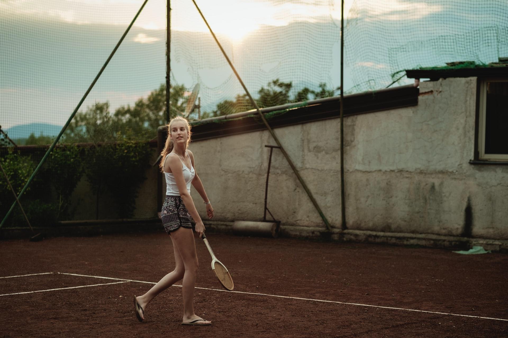 Eine Frau spielt Tennis auf einem Hartplatz während hinter ihr die Sonne hinter den Wolken hervorscheint