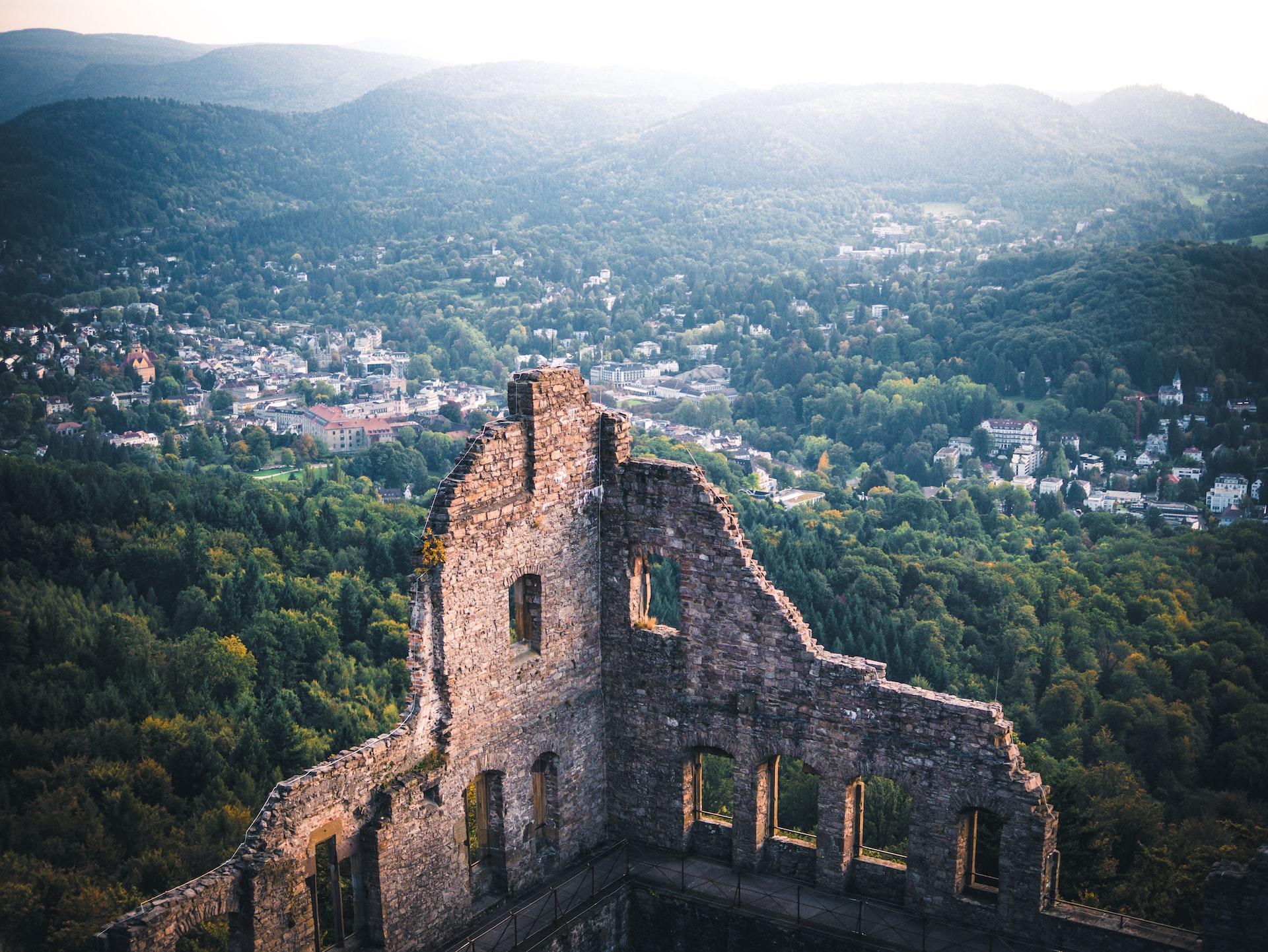 Eine alte Steinmauer thront über einem Tal mit Häusern und Bäumen. 