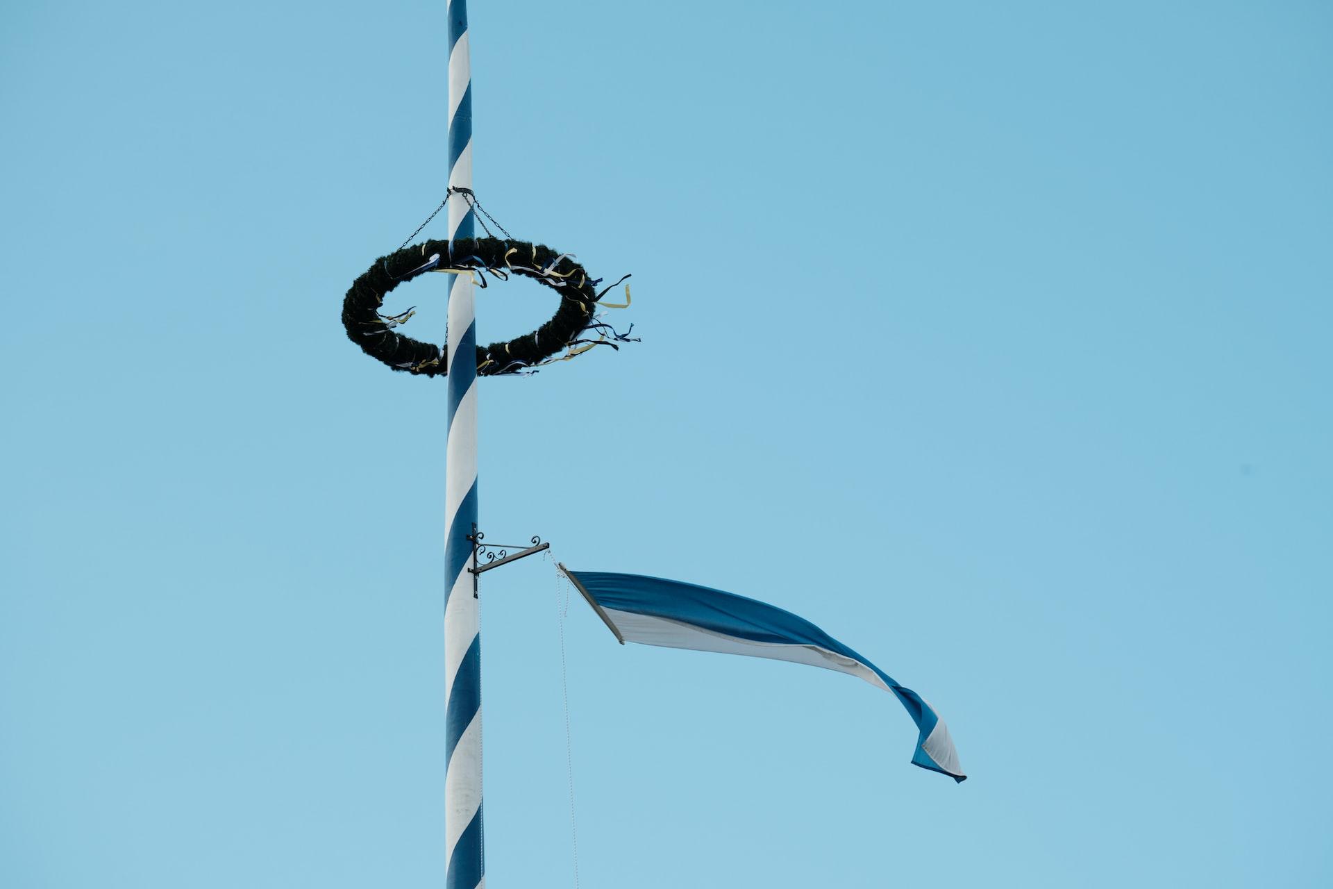 Vor blauem Himmel steht ein blau weiß gestreifter Maibaum.