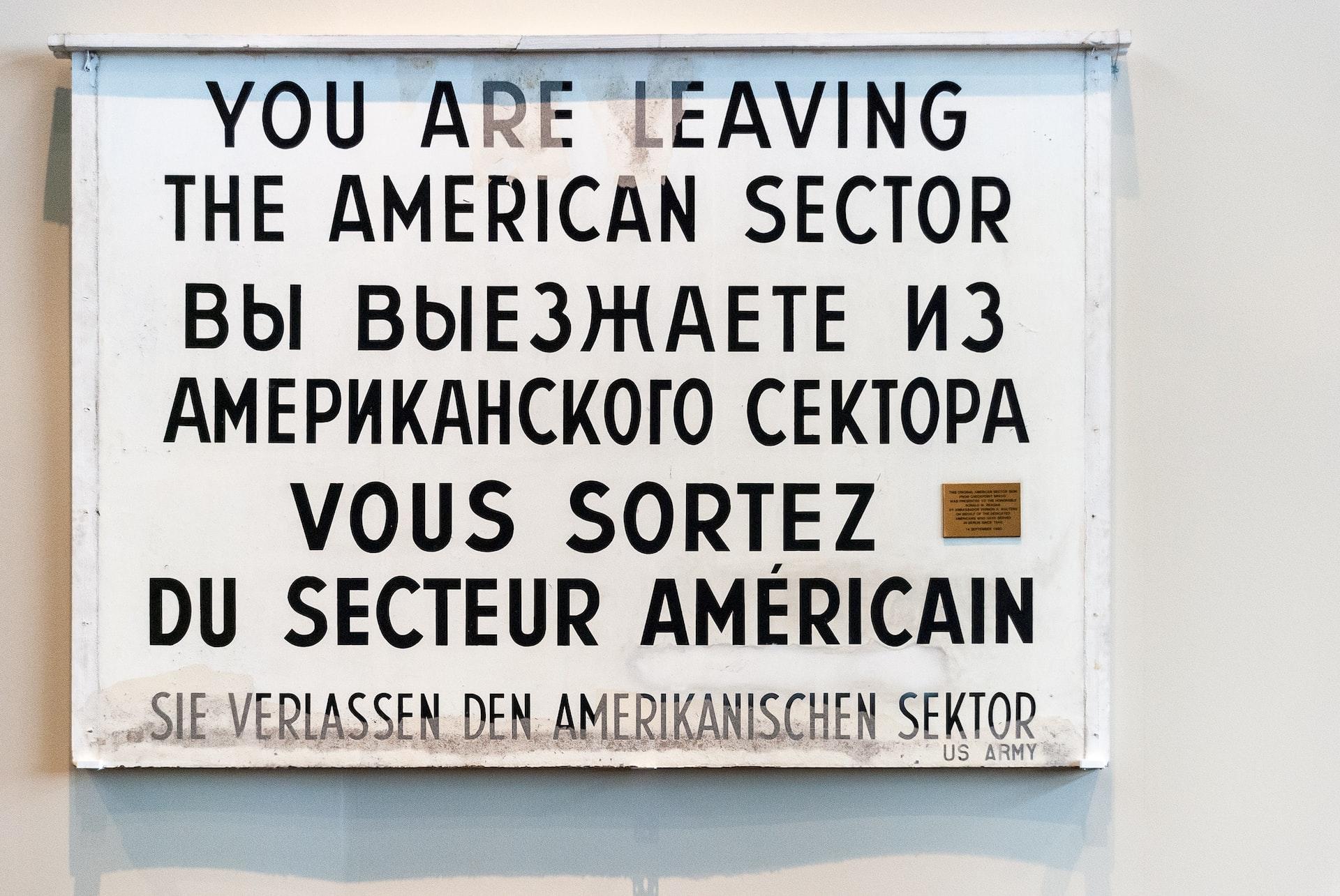 Auf einem weißen Schild steht etwas in schwarzer Schrift in vier verschiedenen Sprachen.