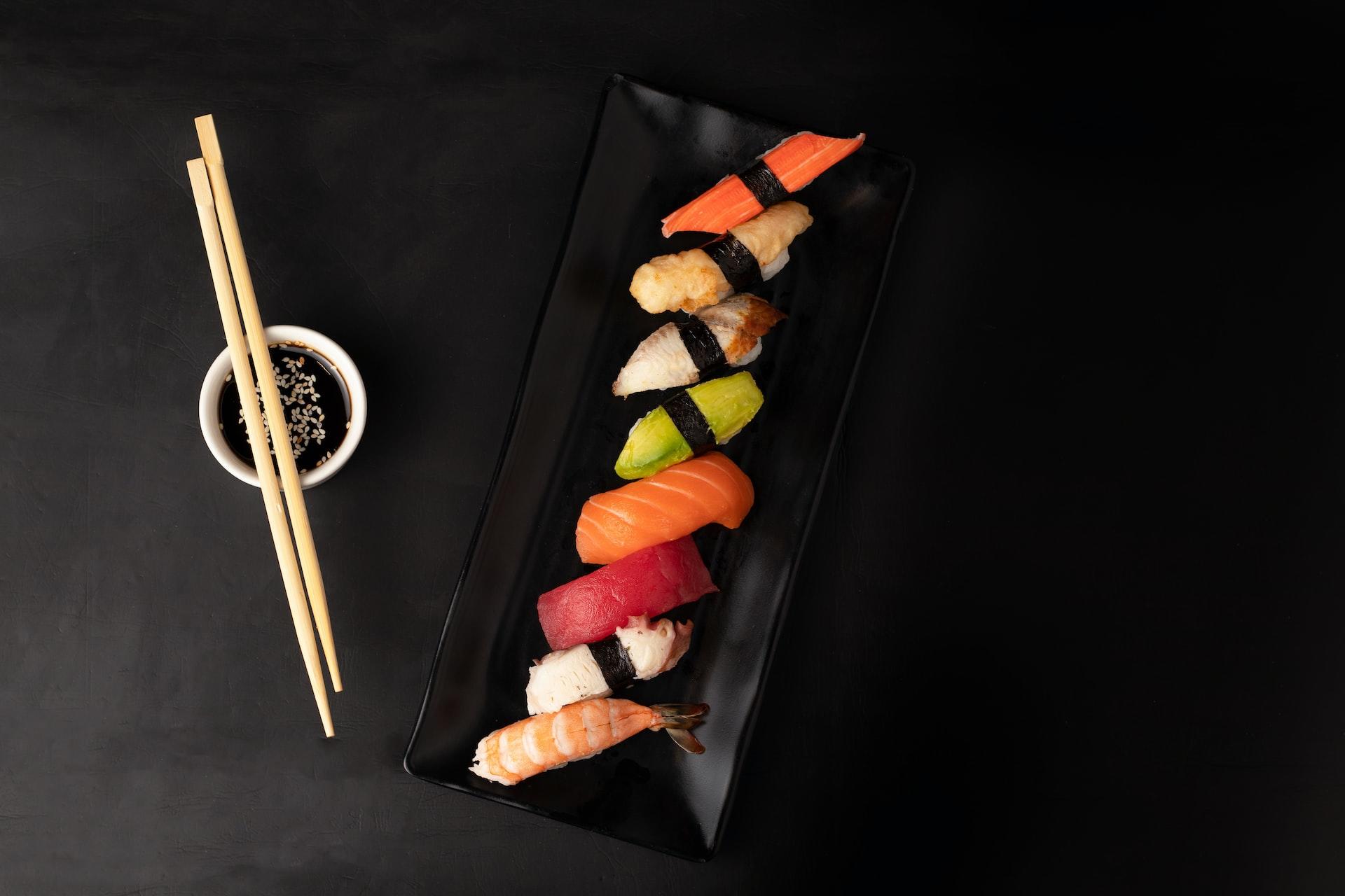 Auf einem schwarzen Untergrund liegen Sushi und zwei Essstäbchen nebeneinander.