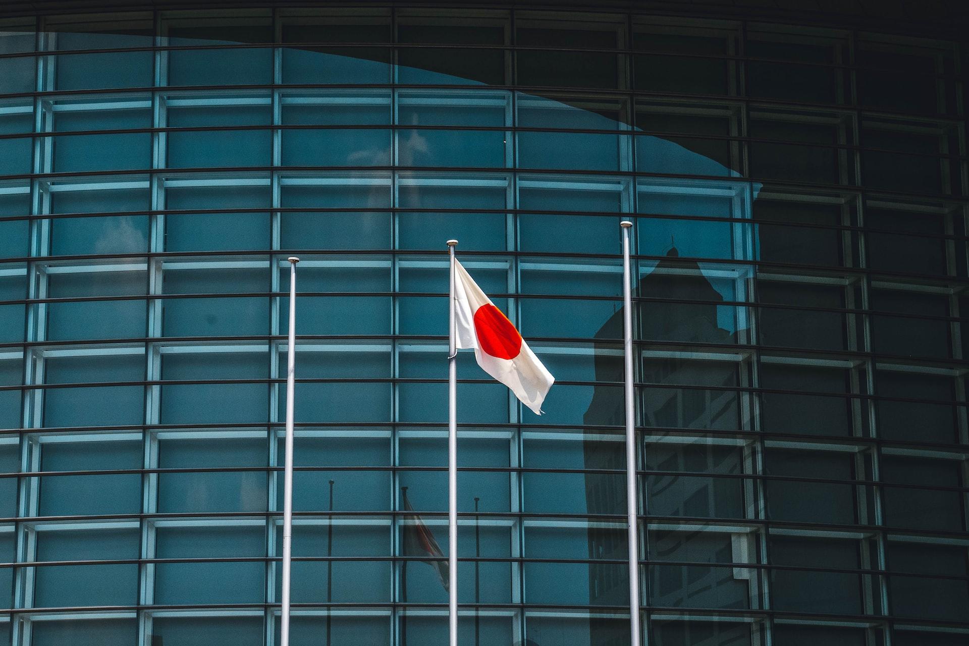Vor einem modernen Gebäude mit Glasfront weht die japanische Flagge im Winden.