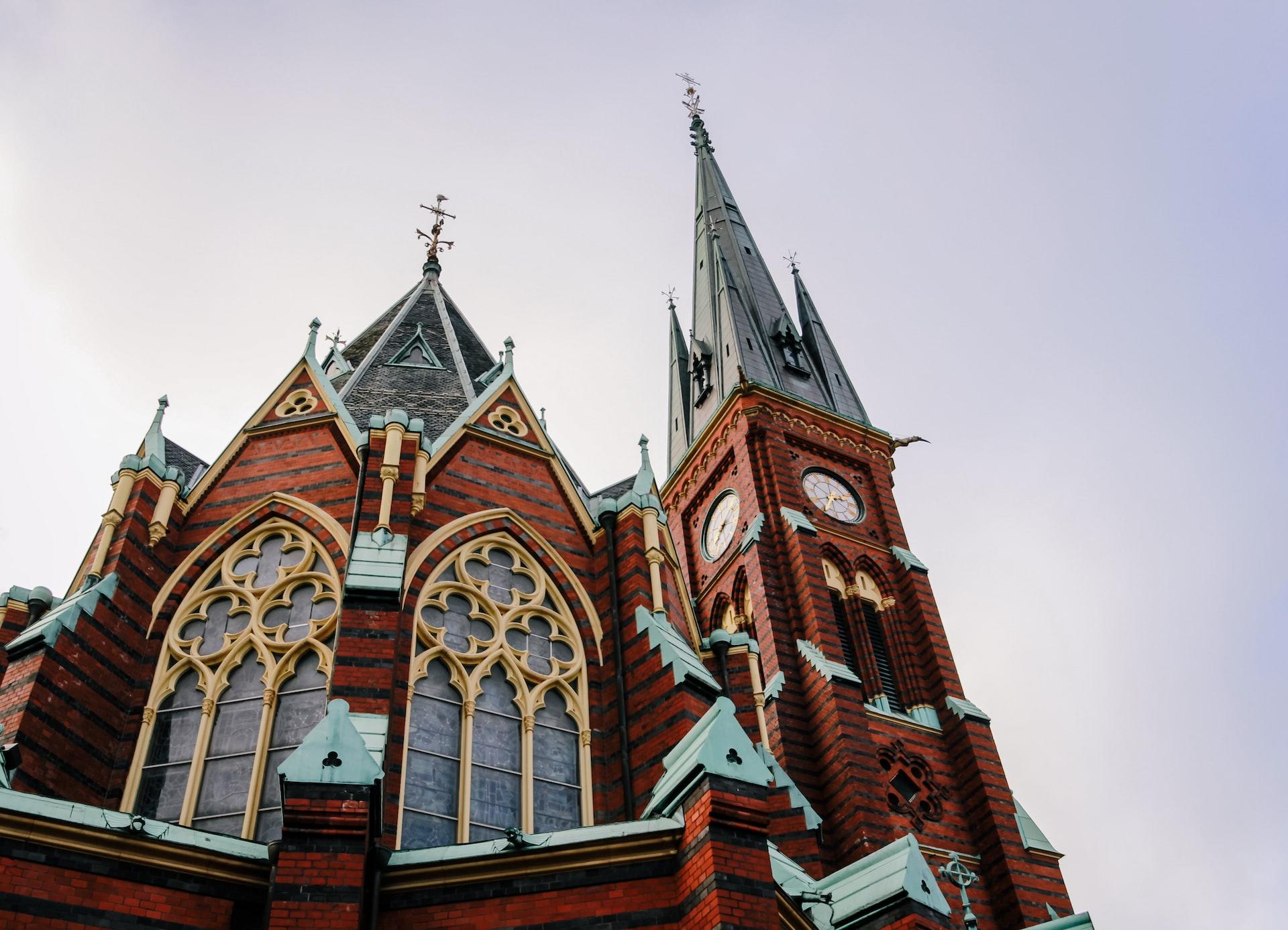 Eine Kirche mit roten Steinen steht vor einem blau grauen Himmel. 