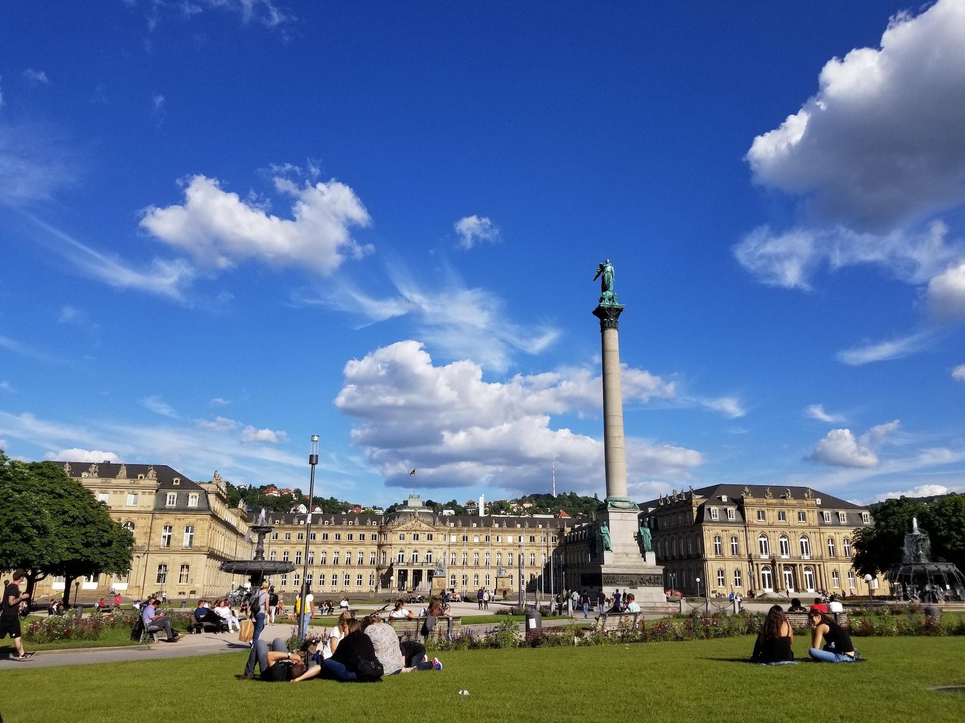 Menschen sitzen auf einer Wiese vor einem Schloss in Stuttgart.
