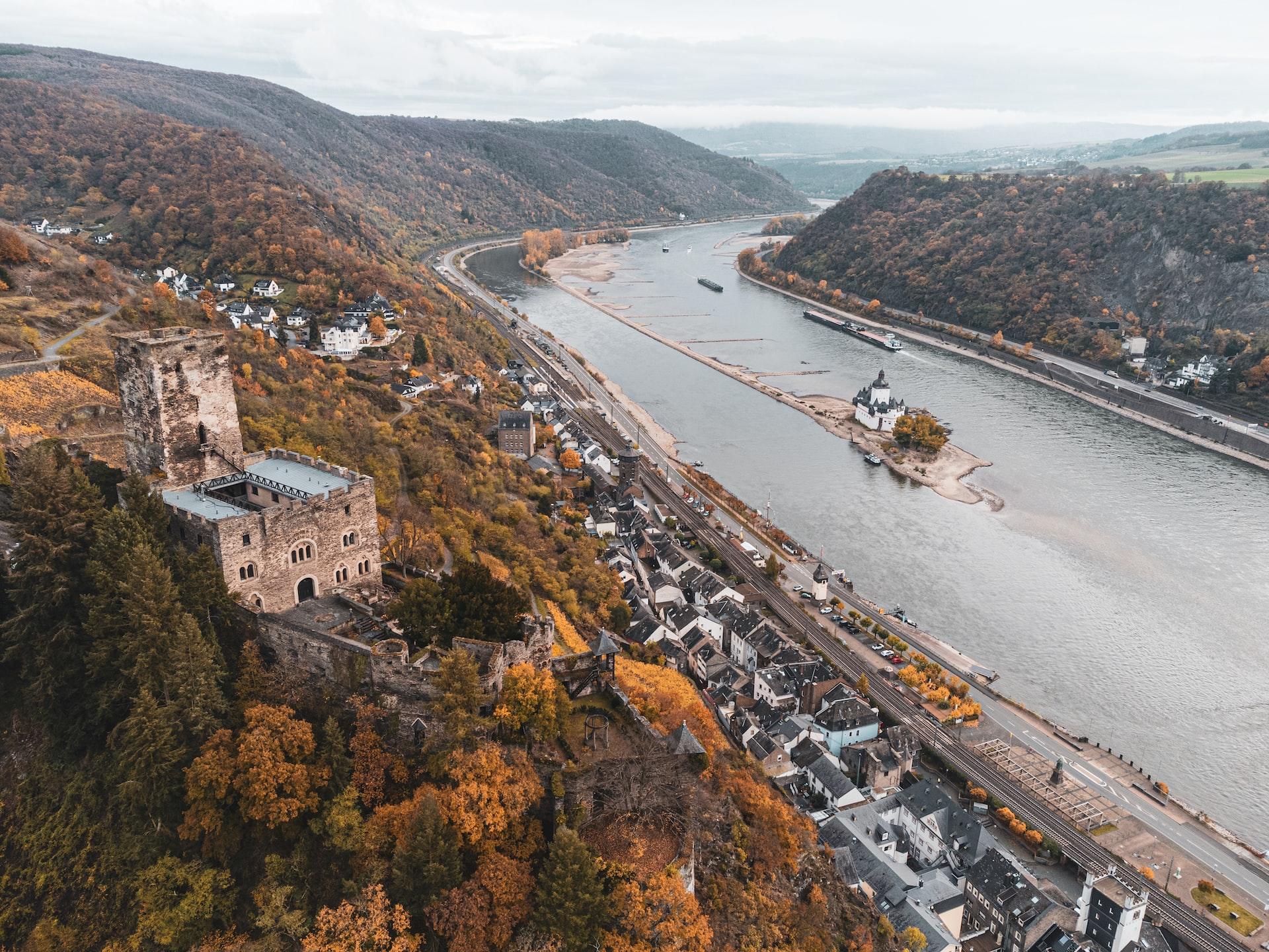 Der Rhein fließt durch ein Tal und links am Hang thront eine Burg.