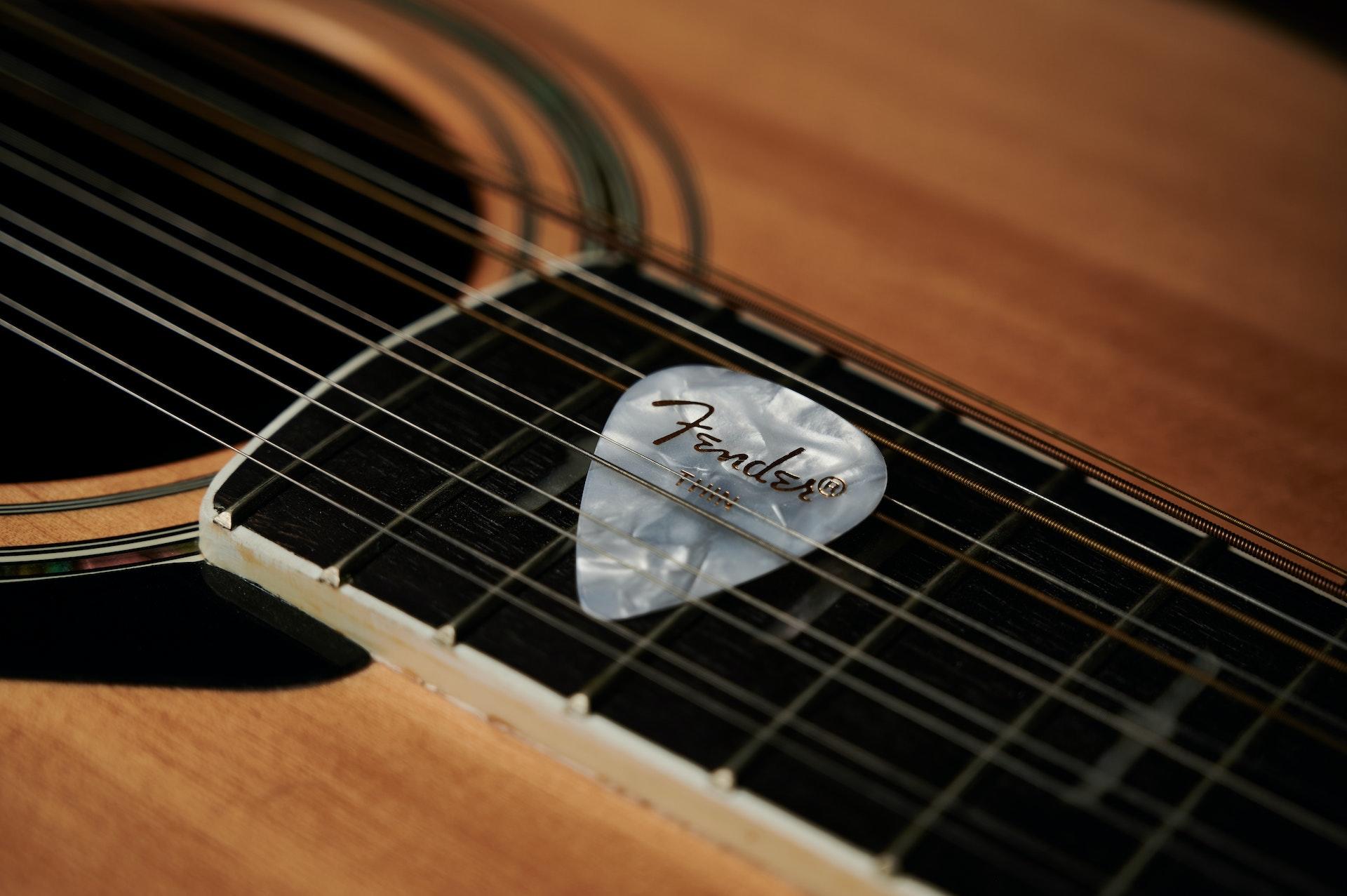 Ein weißes Plektrum ist zwischen die Saiten einer Akustikgitarre geklemmt.