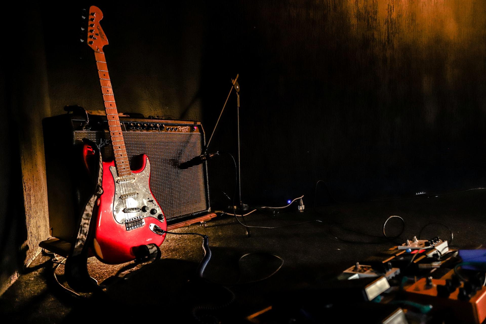 Eine E-Gitarre steht in einem dunklen Raum an einen Verstärker gelehnt.