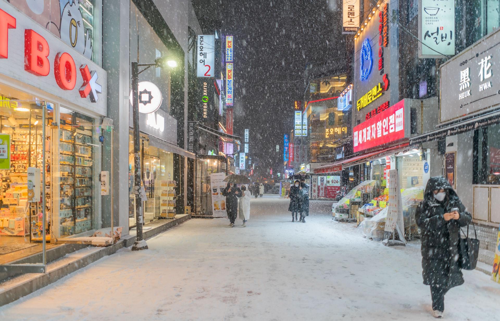 Im Schneefall gehen mehrere Personen durch eine schneebedeckte Straße in Seoul.