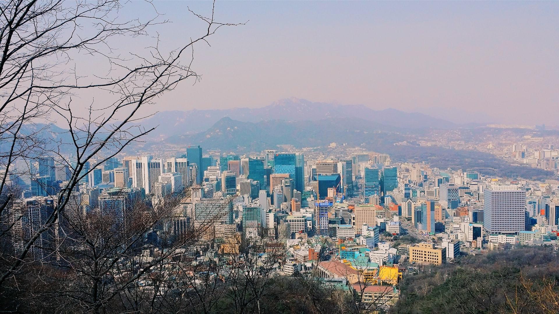 Hinter dem Ausblick über die Stadt Seoul stehen hohe Berge in leichtem Nebel.