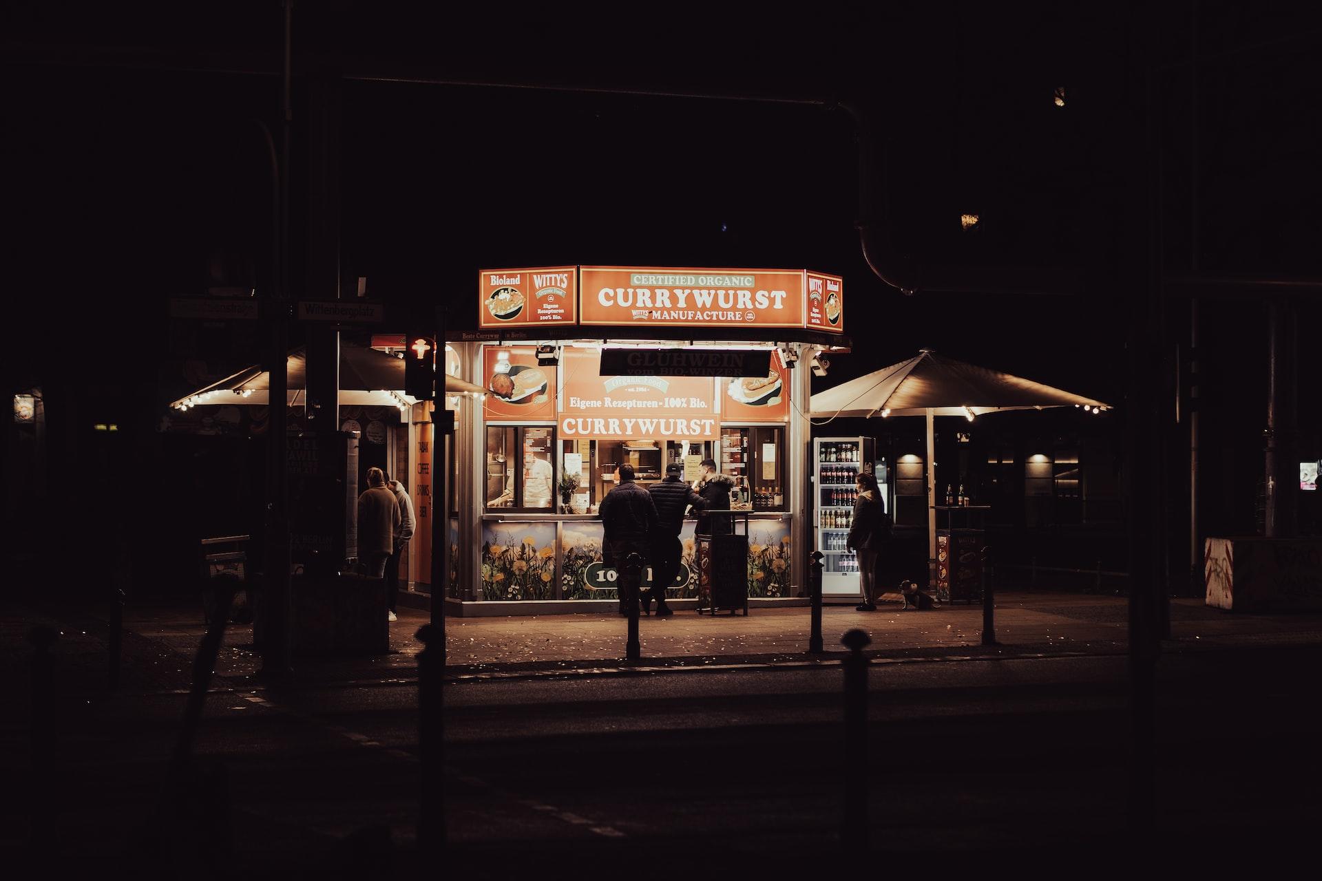 An einem Currywurst Stand stehen einige Leute bei Nacht an.