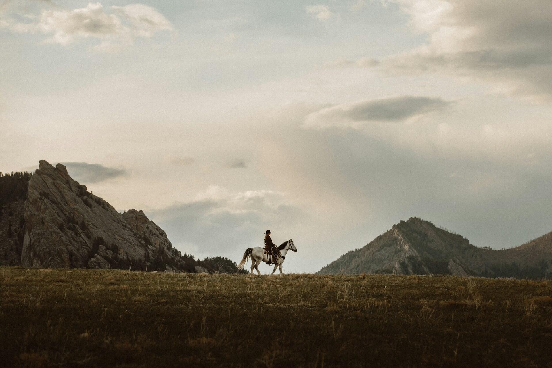 Frau mit Hut auf Pferd vor Bergen auf Wiese.