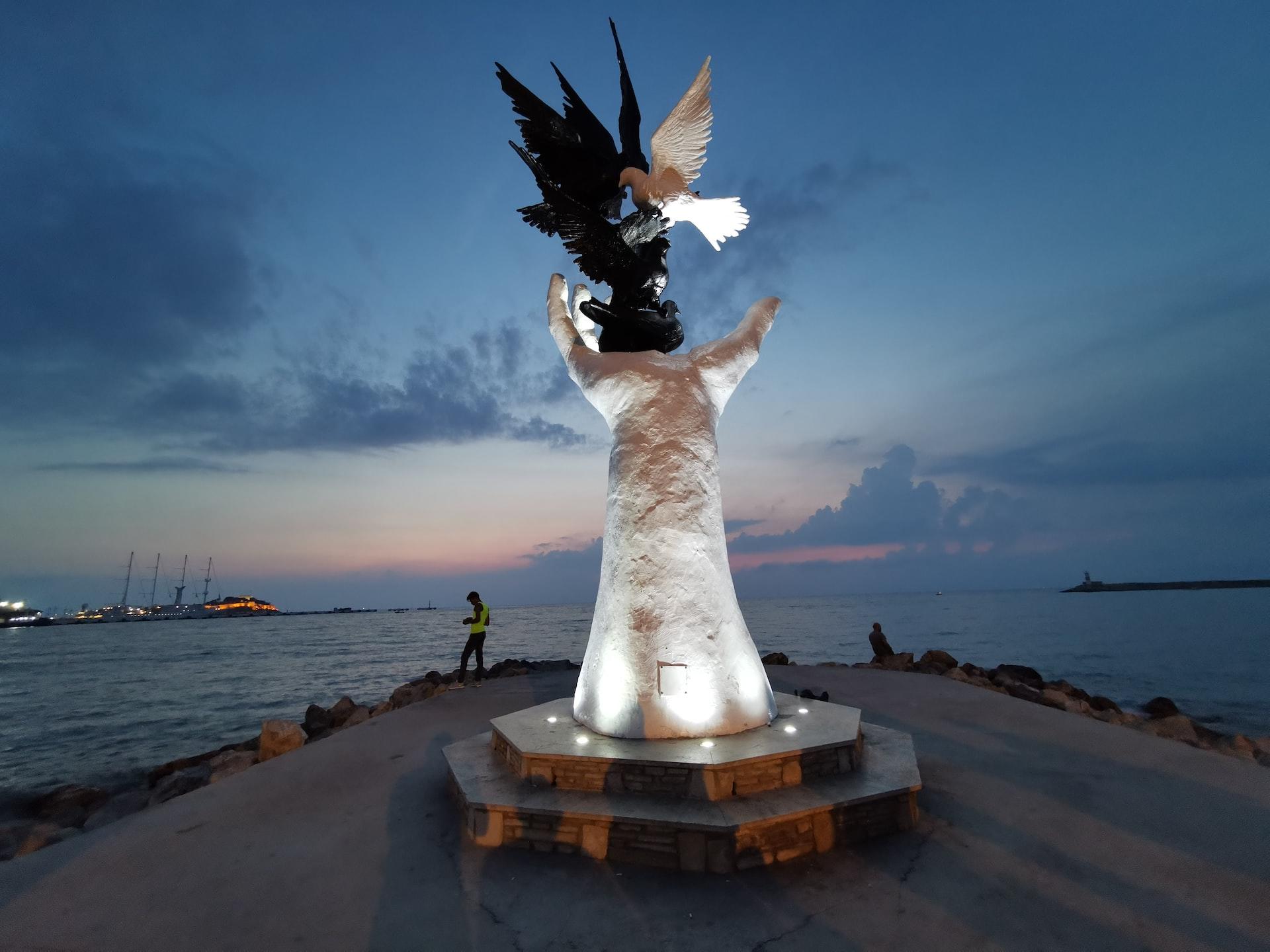 Die Statue einer geöffneten Hand und mehrerer Vögel ist in der Nach beleuchtet.