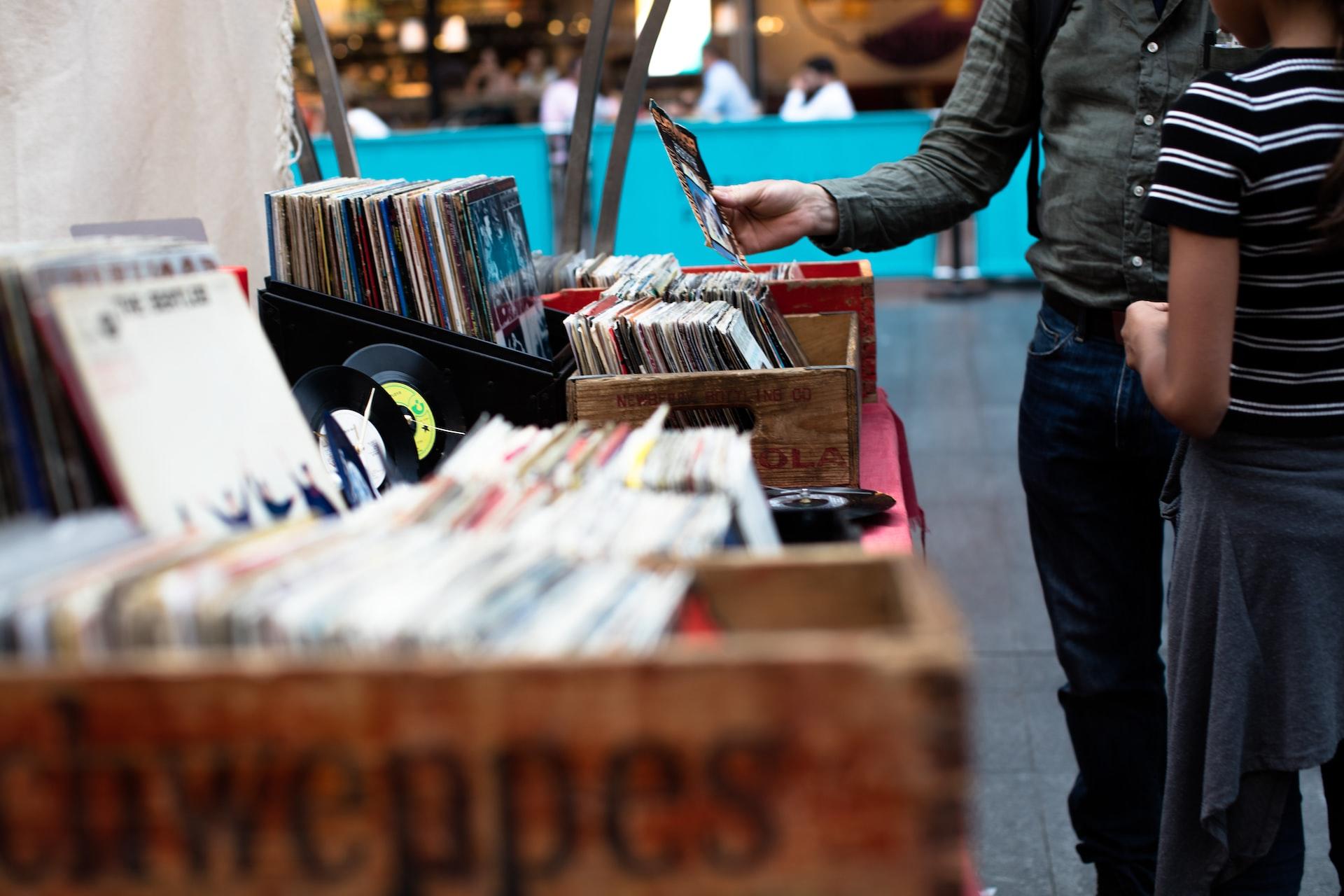 Auf einem Markt steht eine Kiste mit Schallplatten und eine Person steht davor.