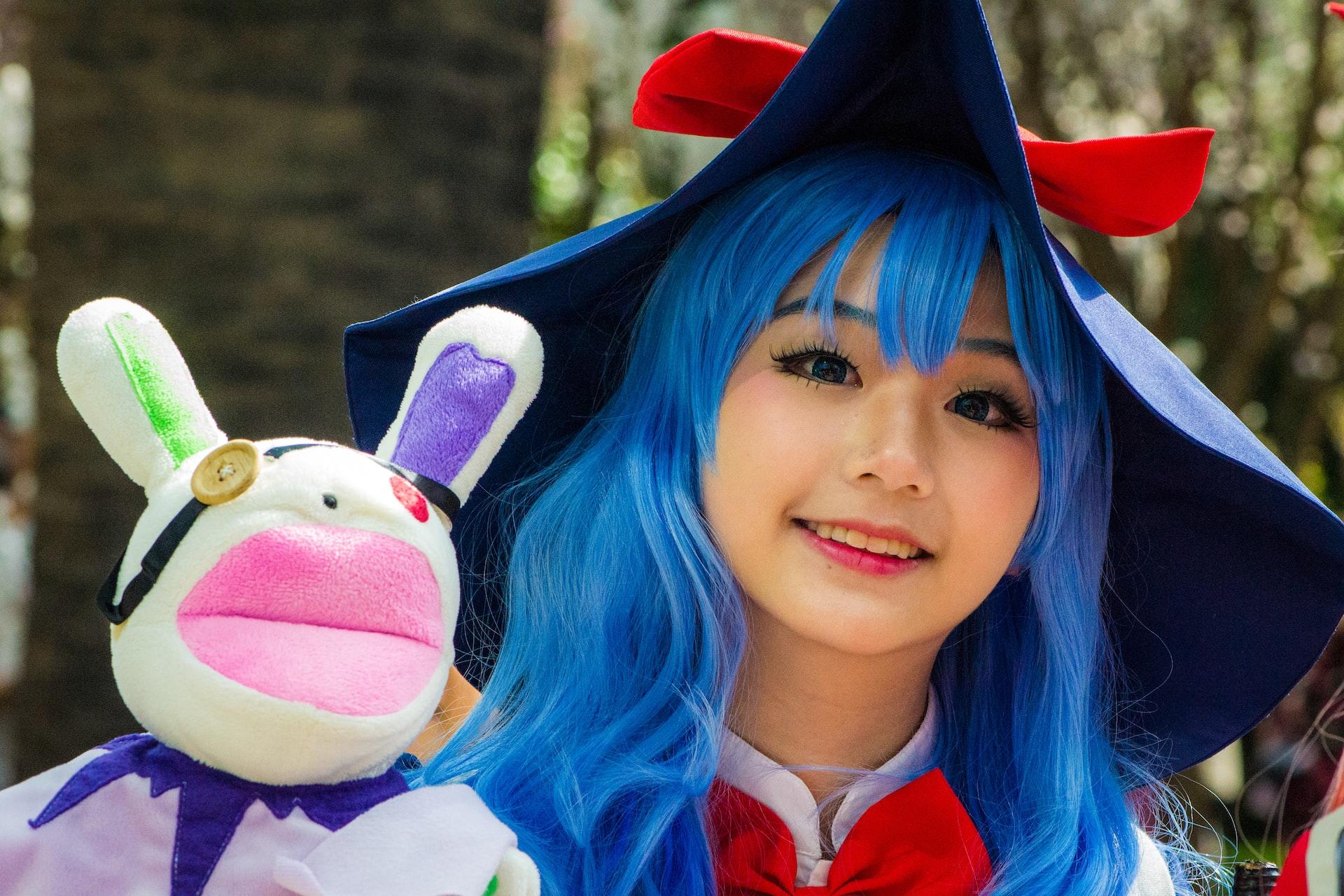 Eine Person mit blauen Haaren hält ein Plüschtier mit langen Ohren neben sich.