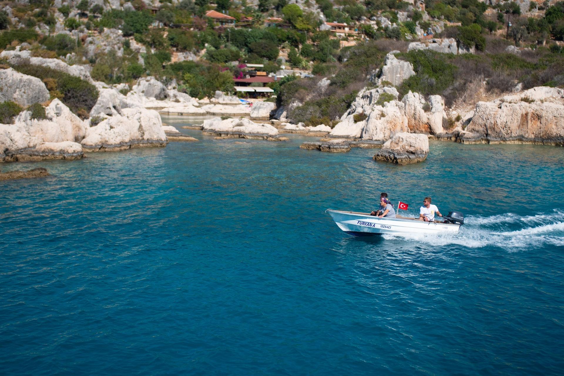 Vor einer felsigen und bewachsenen Küste fährt ein Motorboot mit zwei Personen. 