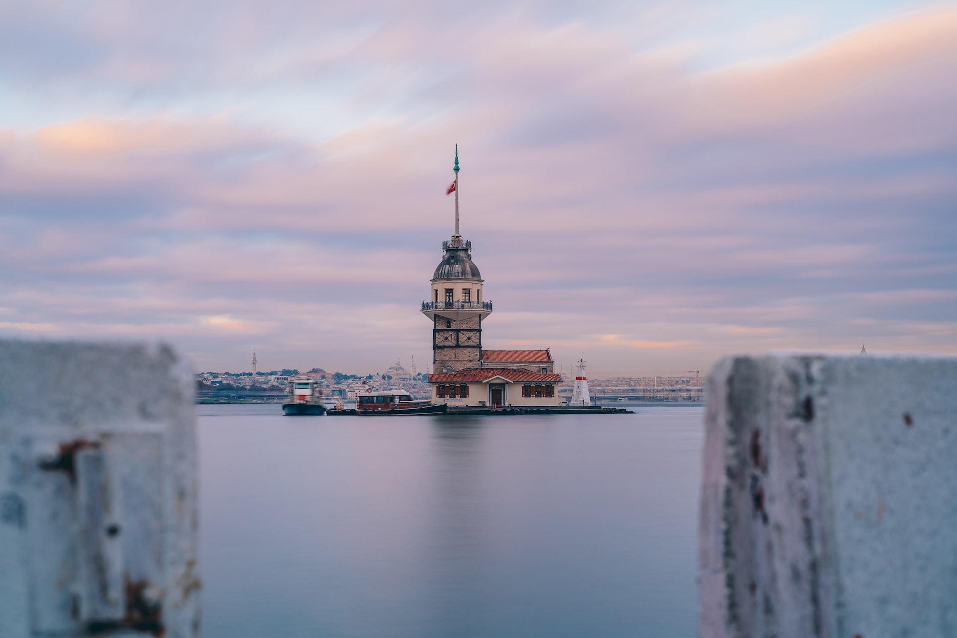 Hinter einer Maueröffnung liegt eine kleine Insel mit einem Leuchtturm im Wasser.