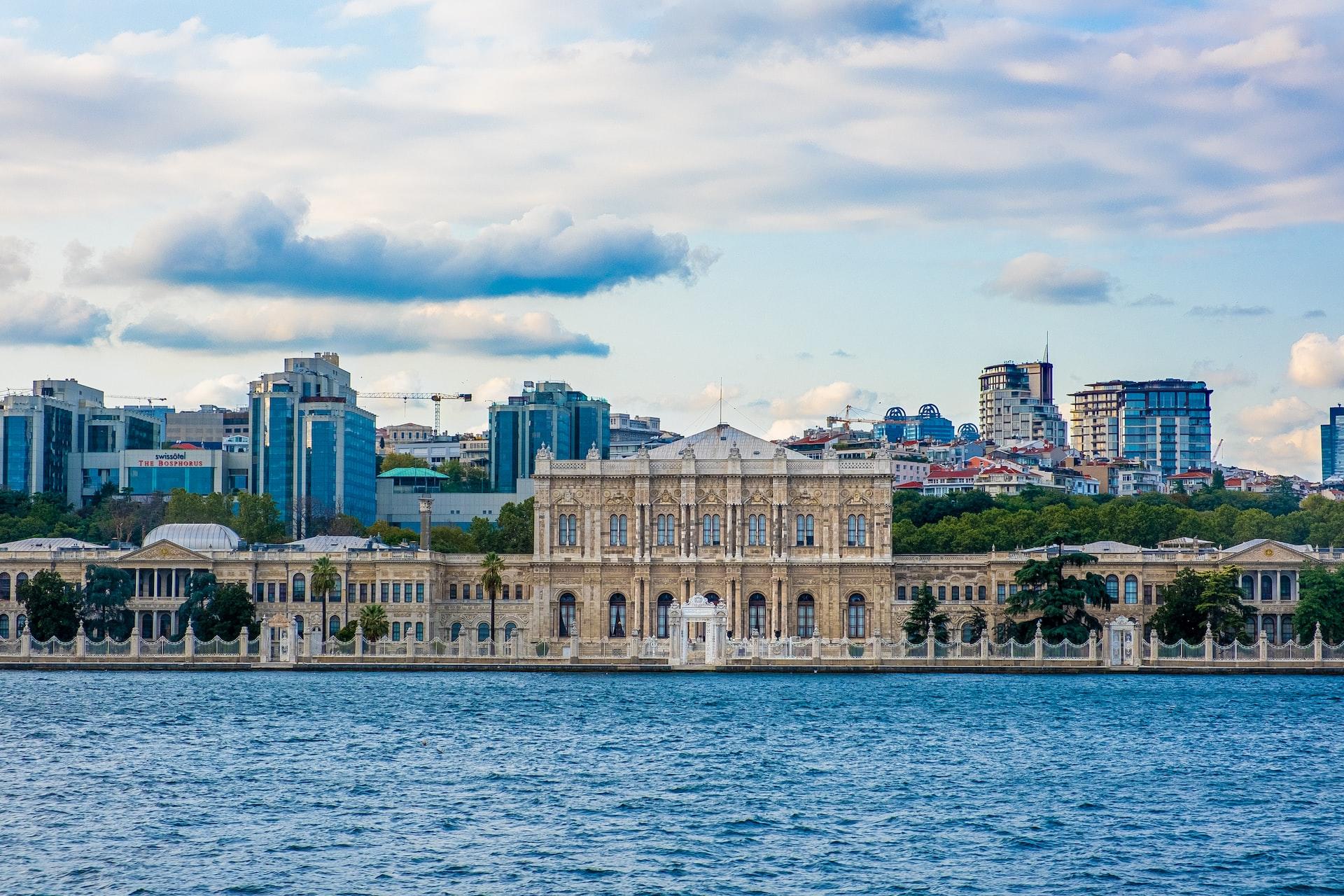 Hinter dem Wasser steht ein weißer Palast und dahinter erhebt sich die Stadt.