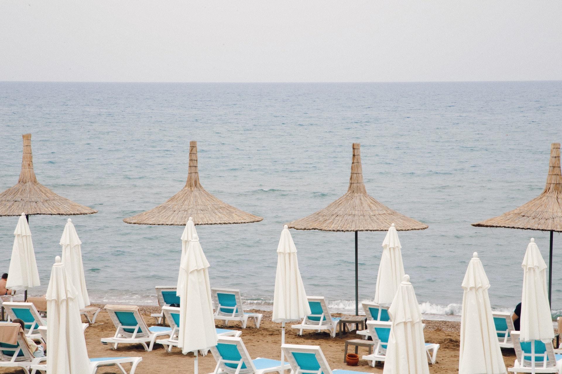 Liegestühle stehen an einem Strand und daneben sind geöffnete und geschlossene Sonnenschirme.
