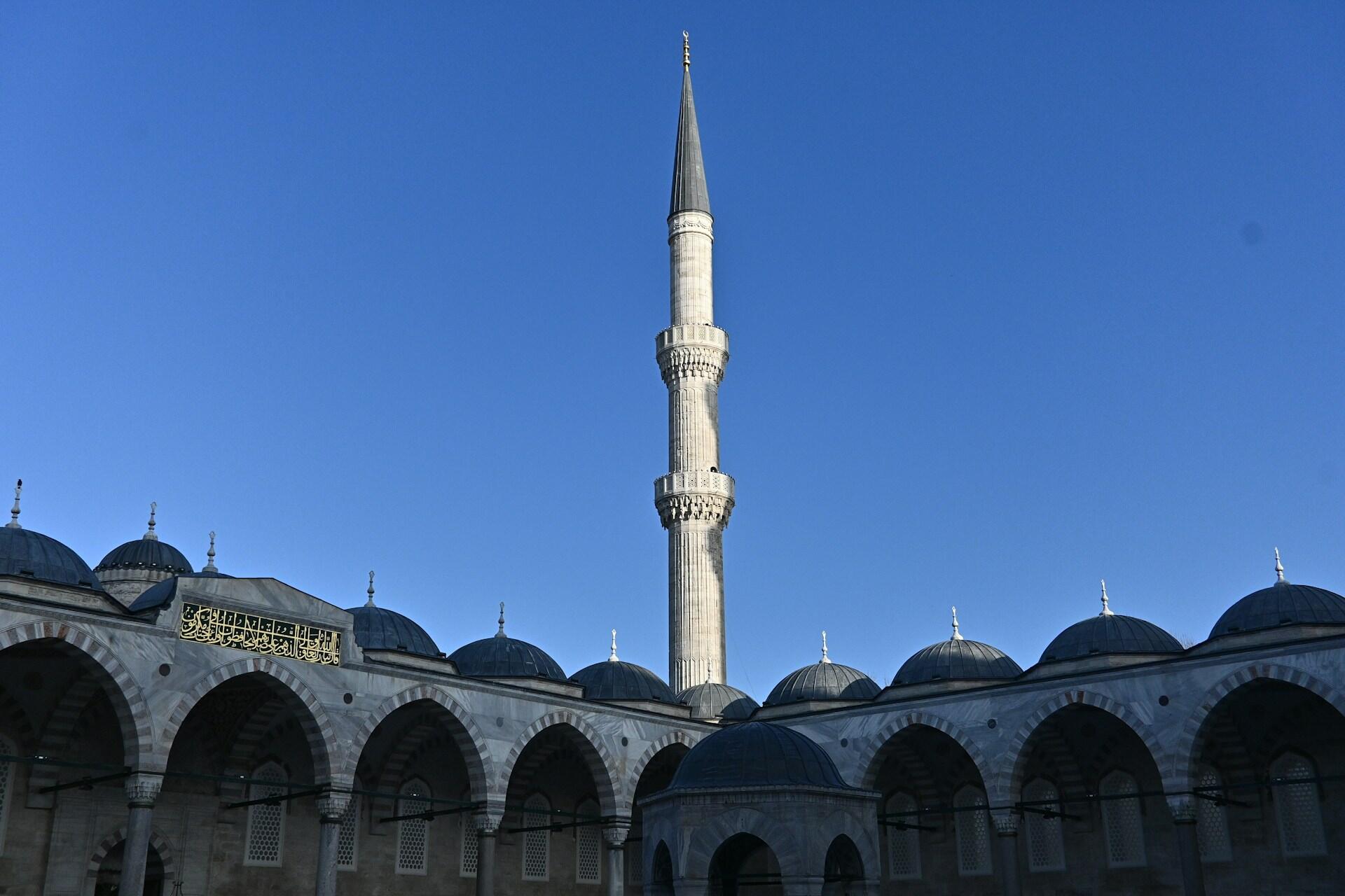 Innenhof einer Moschee mit Turm vor blauem Himmel.