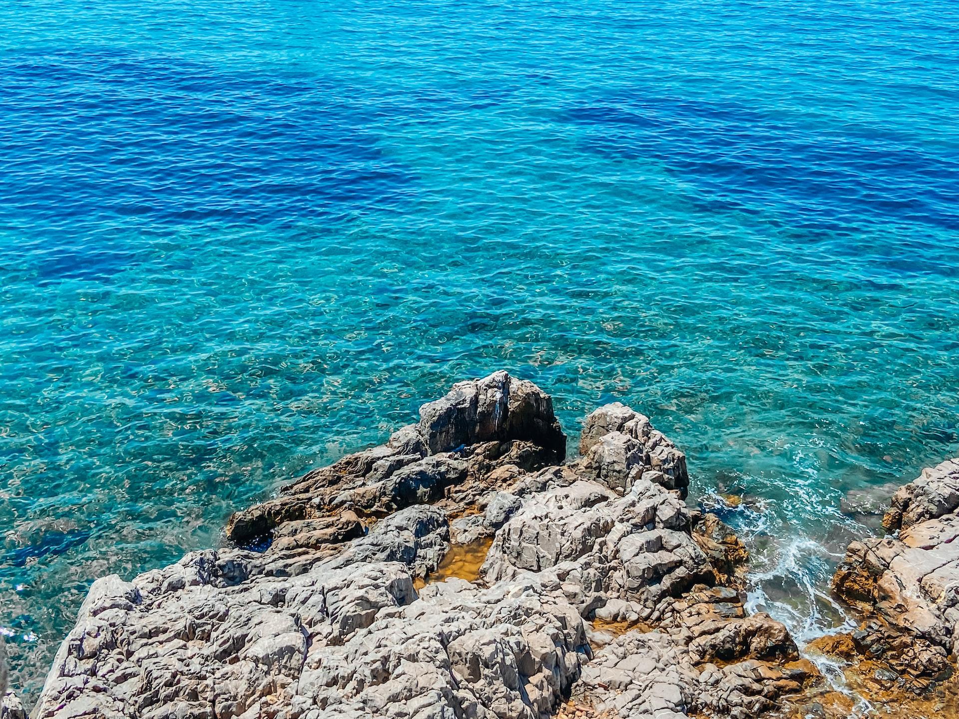 Ein grauer Fels mit vielen Klüften ragt in türkisblaues Wasser hinein.