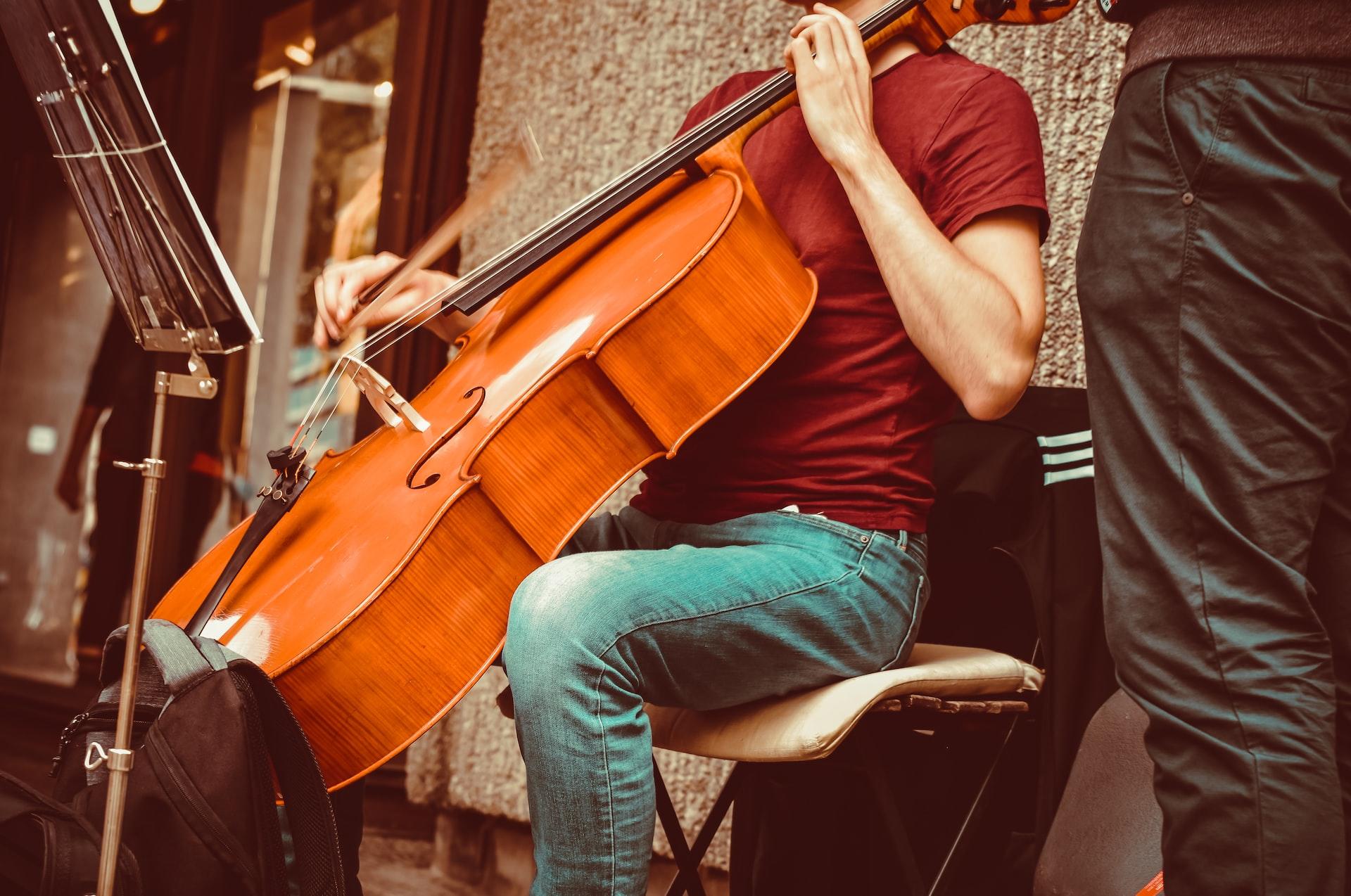Eine Person sitzt vor einem Notenständer und hält ein Cello zwischen den Beinen. 