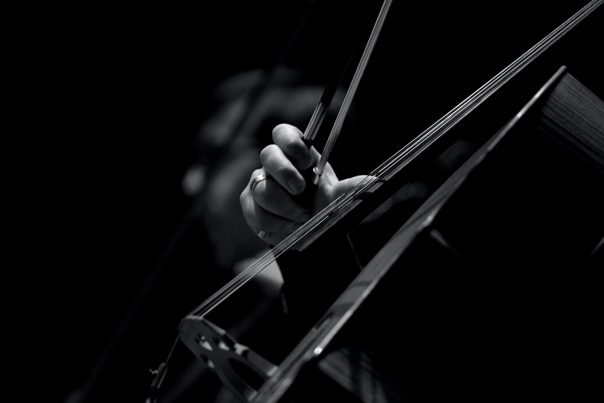 Eine Hand hält einen Streichbogen und zupft mit dem Daumen die Saiten eines Cellos.