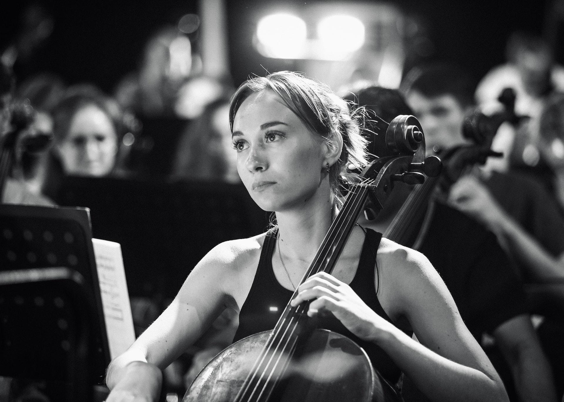 Eine Person sitzt mit einem Cello inmitten anderer Musiker und schaut nach vorne. 