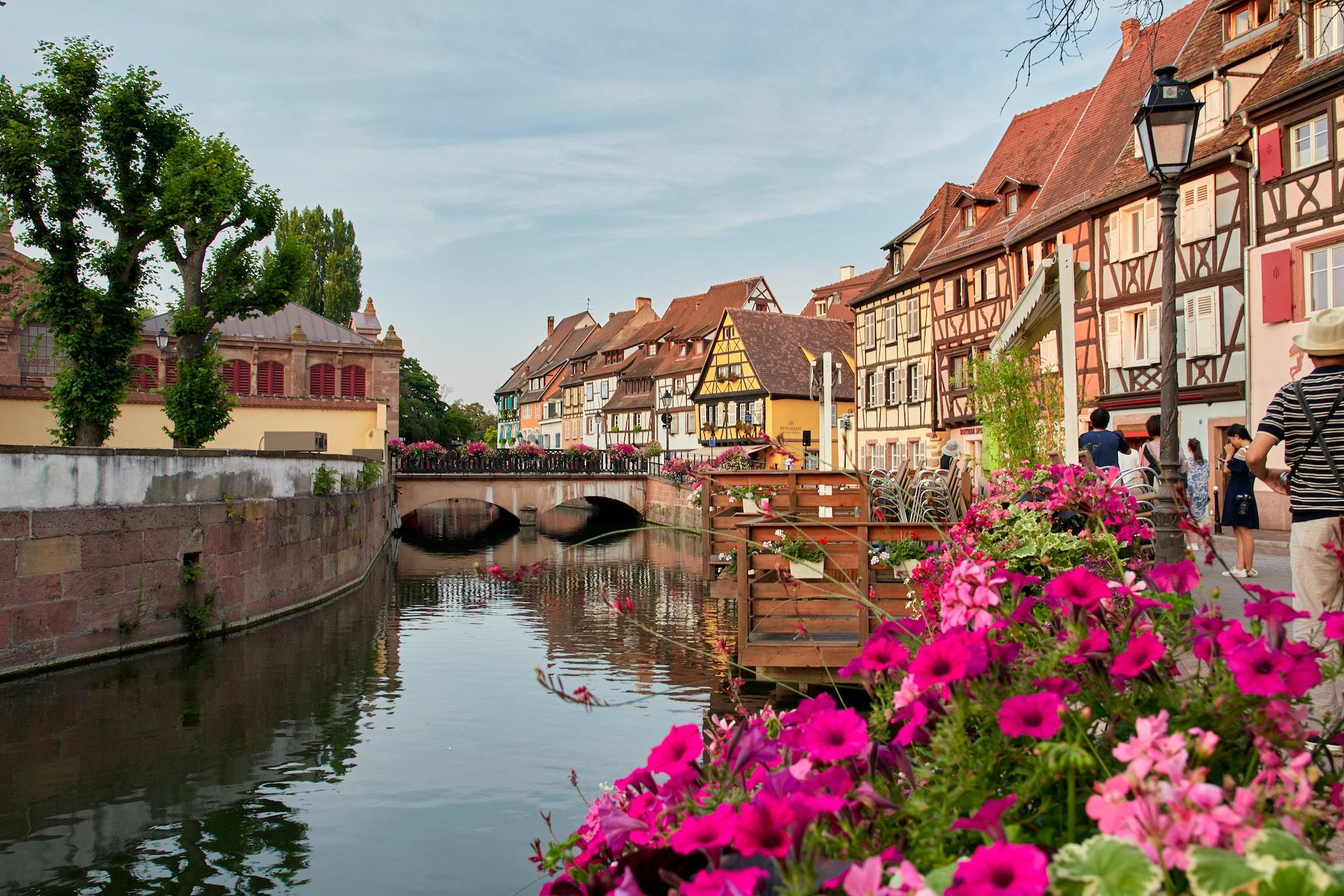 Blick über einen Kanal in einer elsässischen Stadt mit Fachwerkhäusern und Blumen.