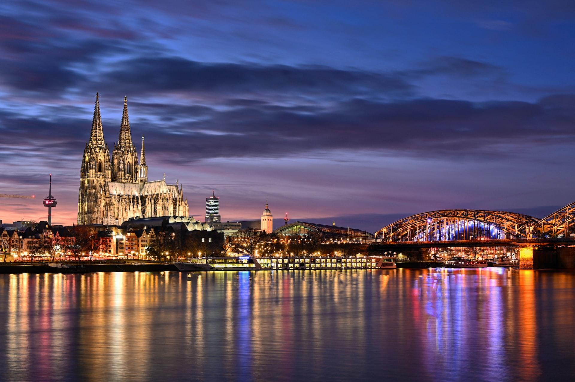 Im Abendlicht sind der Kölner Dom und die Rheinbrücke hell beleuchtet.