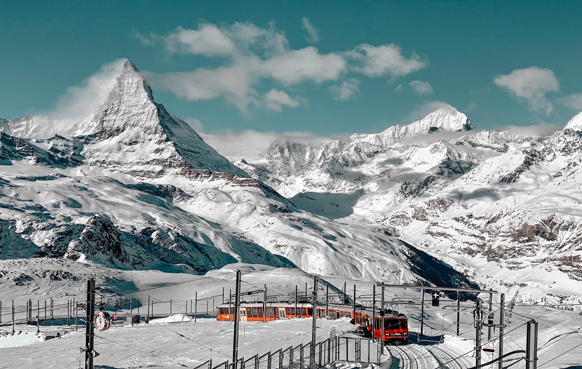 Das Matterhorn wie hier mitten in einer Schneelandschaft durch die ein roter Zug führt ist der berühmtestes Schweizer Berg.