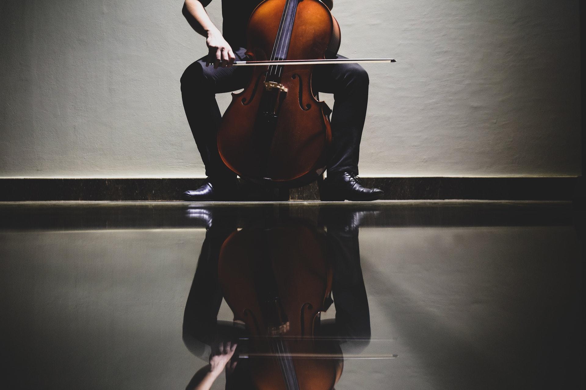 Der Fußboden spiegelt das Bild einer auf einem Stuhl sitzenden und Cello spielenden Person.