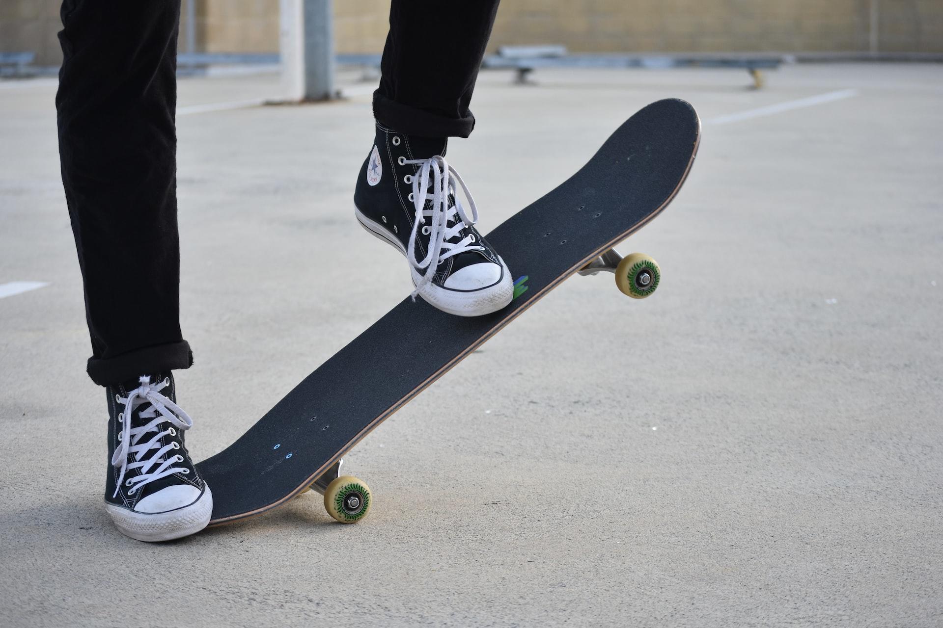 Ein Skatebord wird von einem Fuß auf den Boden gedrückt die andere Seite ragt in die Höhe.