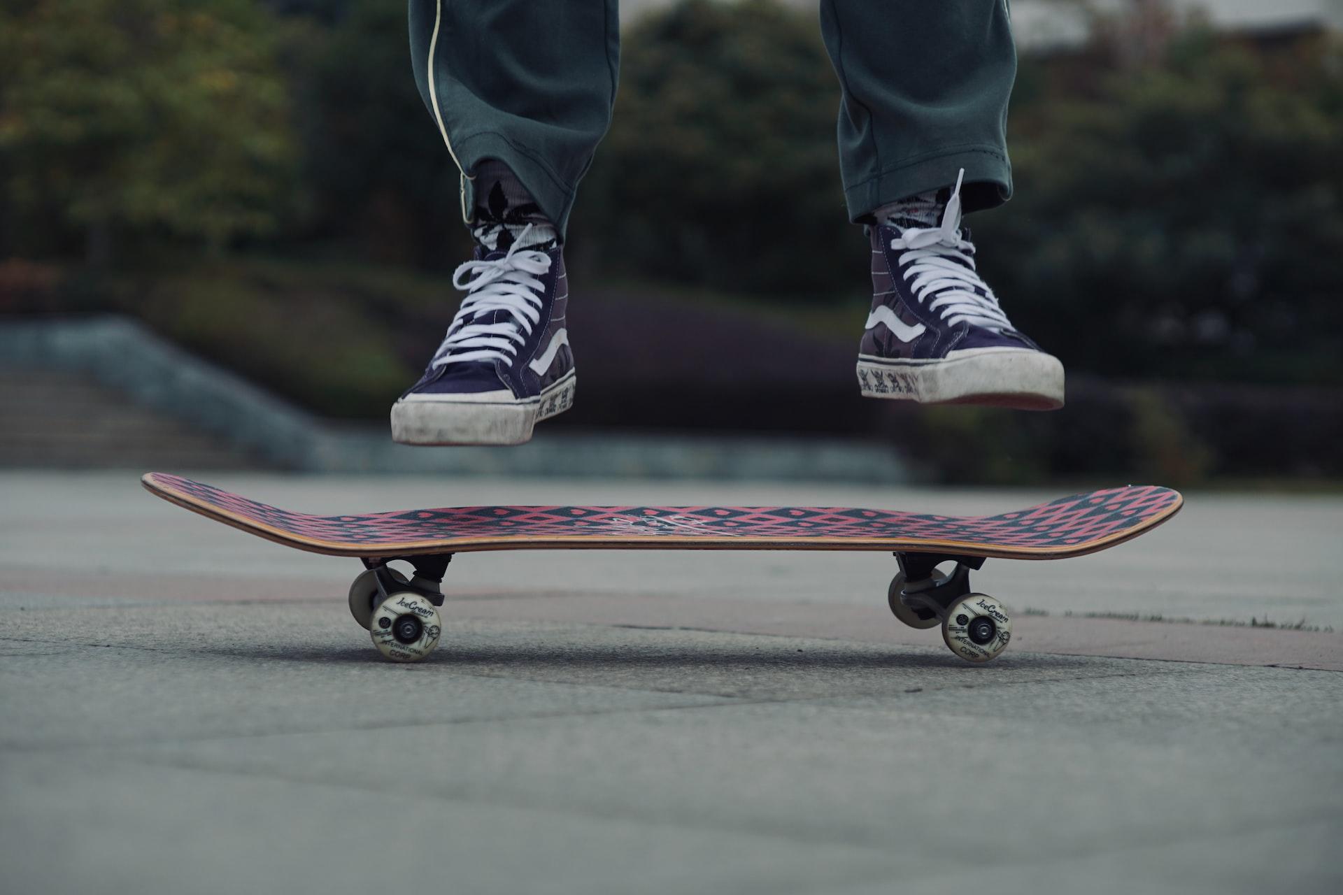 Ein Skateboard steht auf dem Boden und darüber sind zwei Füße in der Luft.
