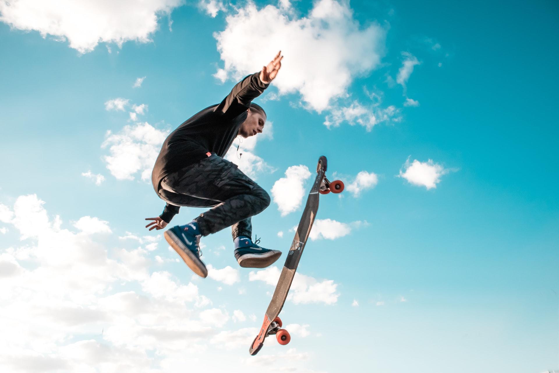 Eine Person ist vor blauem Himmel in der Luft und ein Skateboard schwebt vertikal zu ihrem Körper.